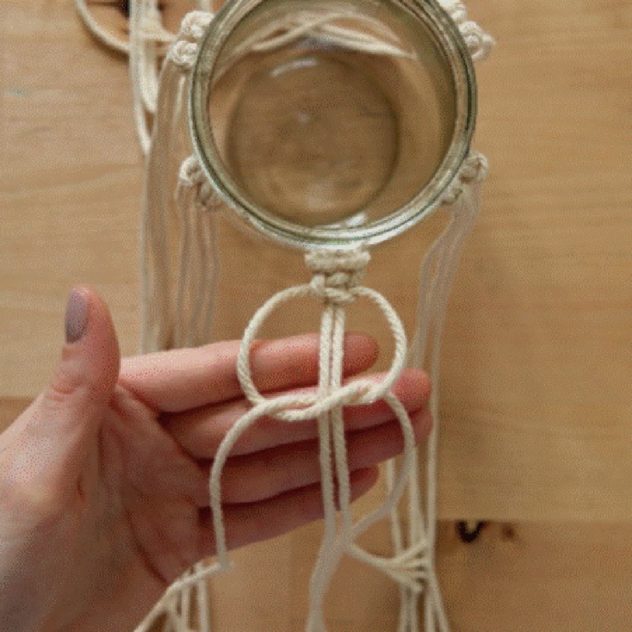 Une main noue un macramé autour d'un bocal en verre.
