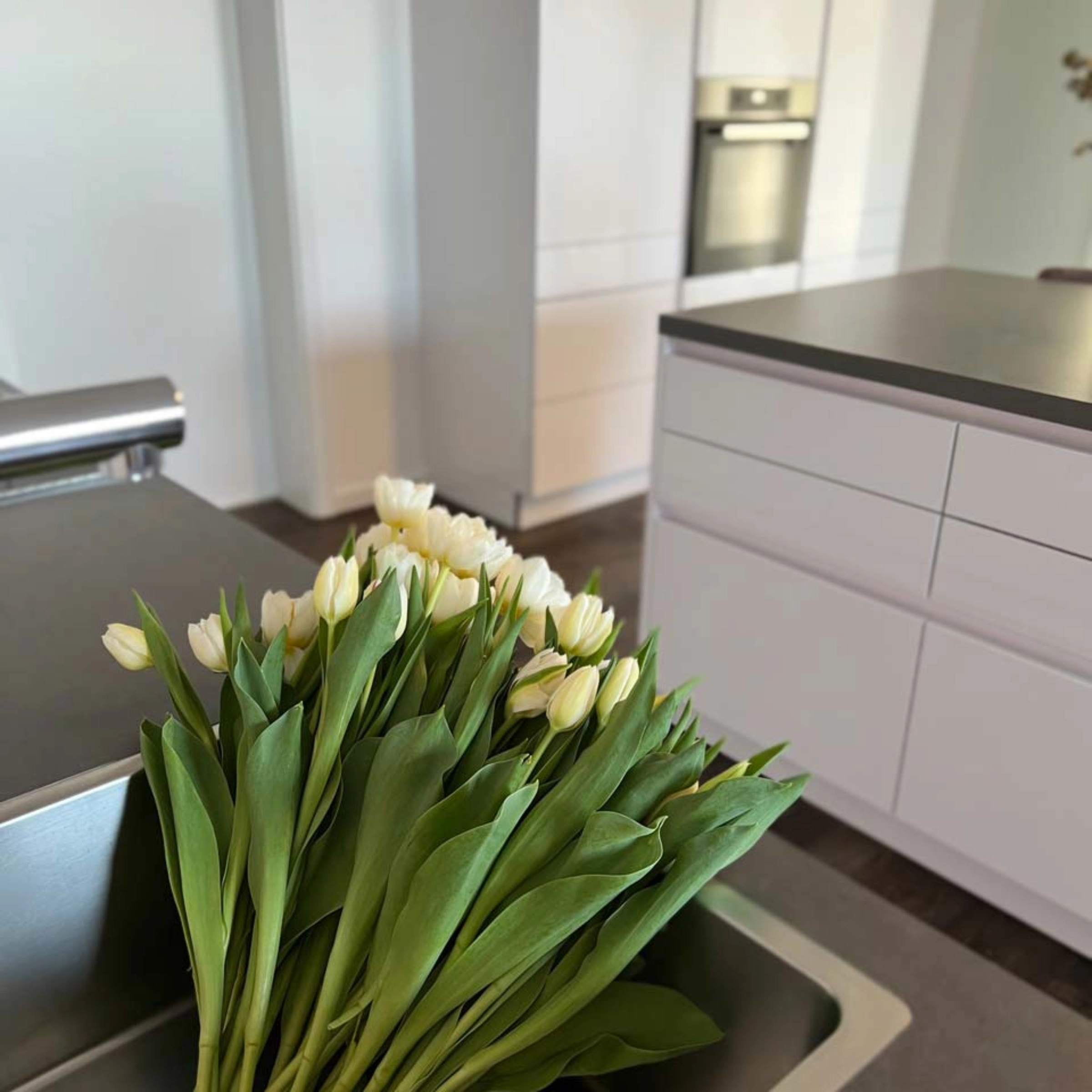 Une cuisine moderne avec des placards blancs et un bouquet de tulipes blanches sur le comptoir. Nolte Kitchen.
