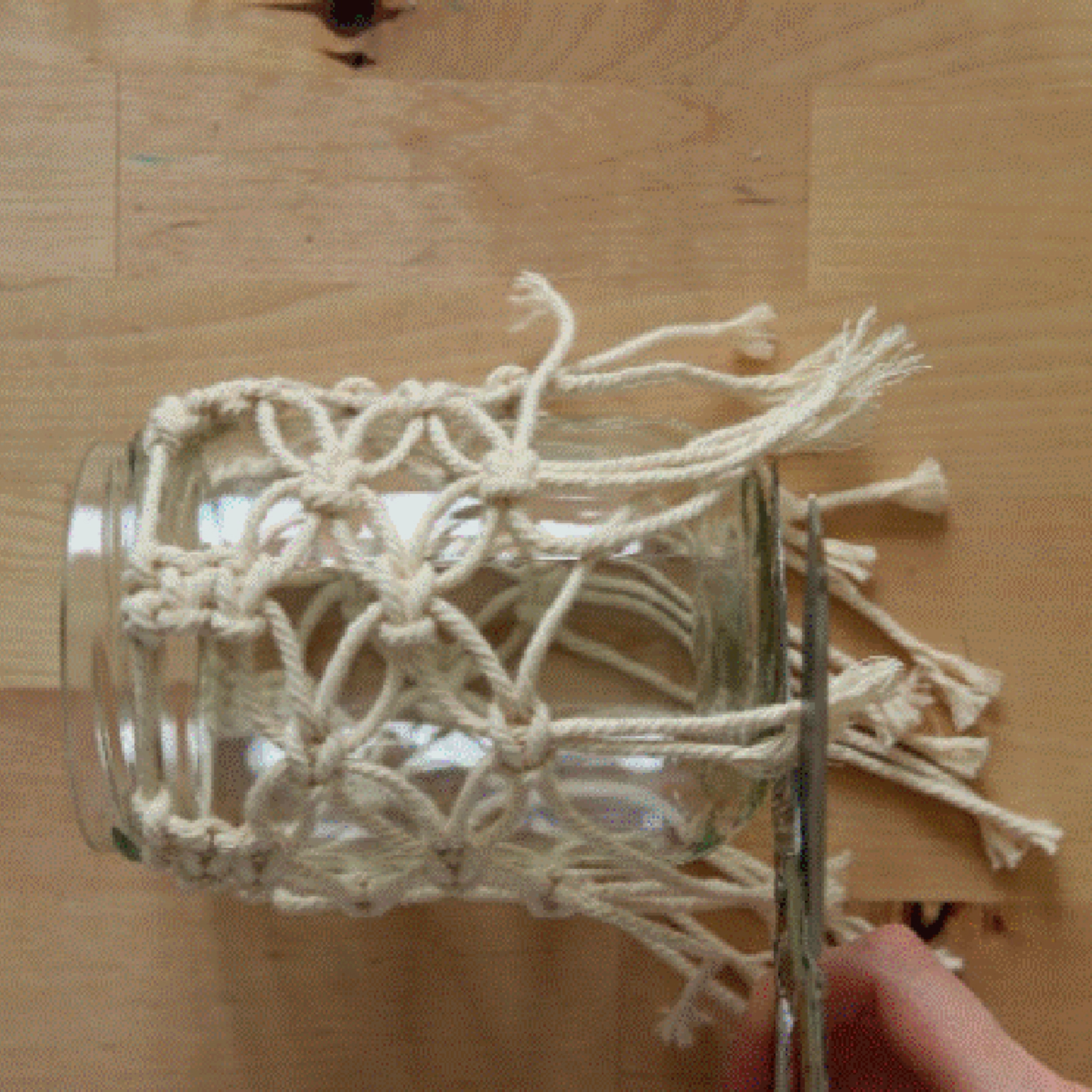 Un verre enveloppé d'un filet en macramé, quelqu'un coupe les fils.