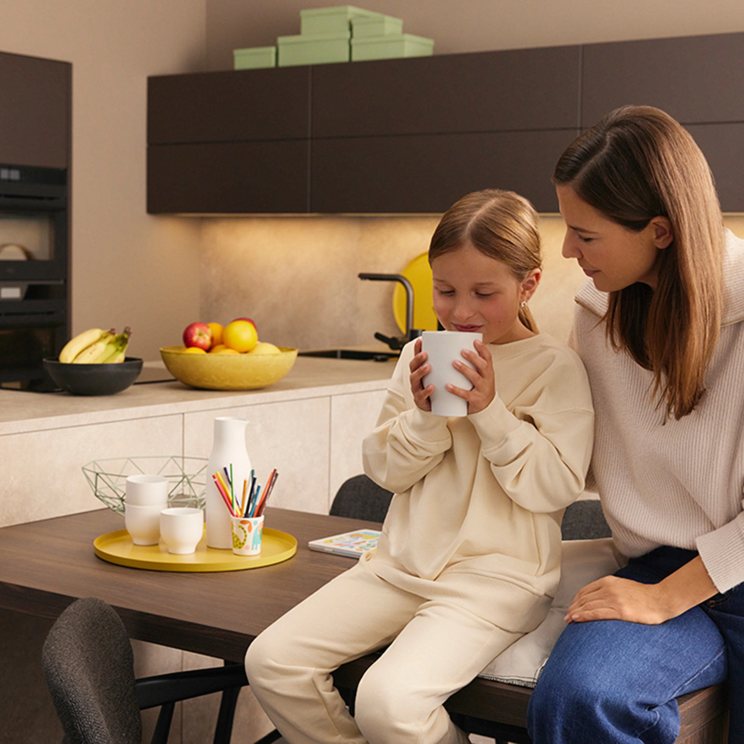 Eine Frau und ein Kind sitzen in einer modernen Küche von Nolte Küchen, das Kind hält eine Tasse.