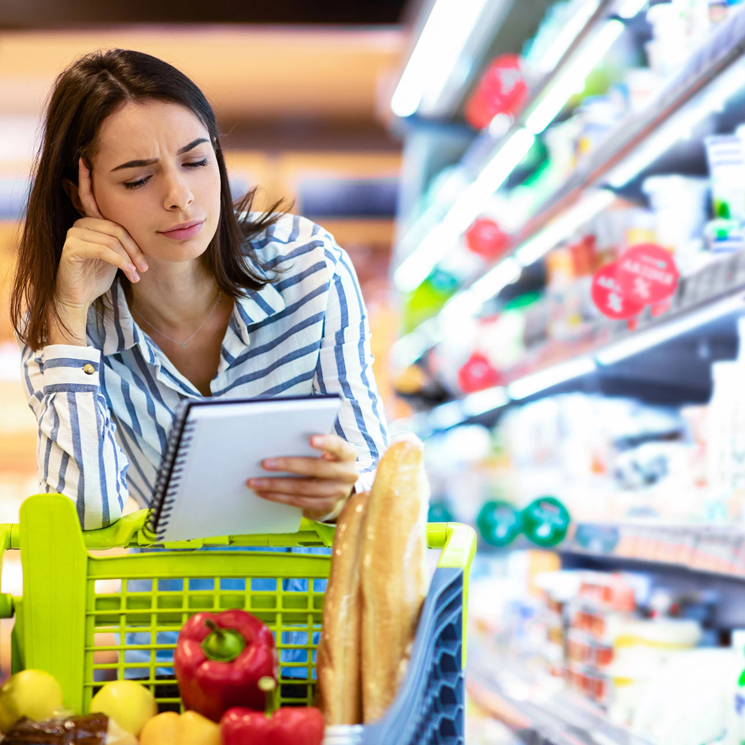 Une femme regarde pensivement une liste de courses au supermarché.