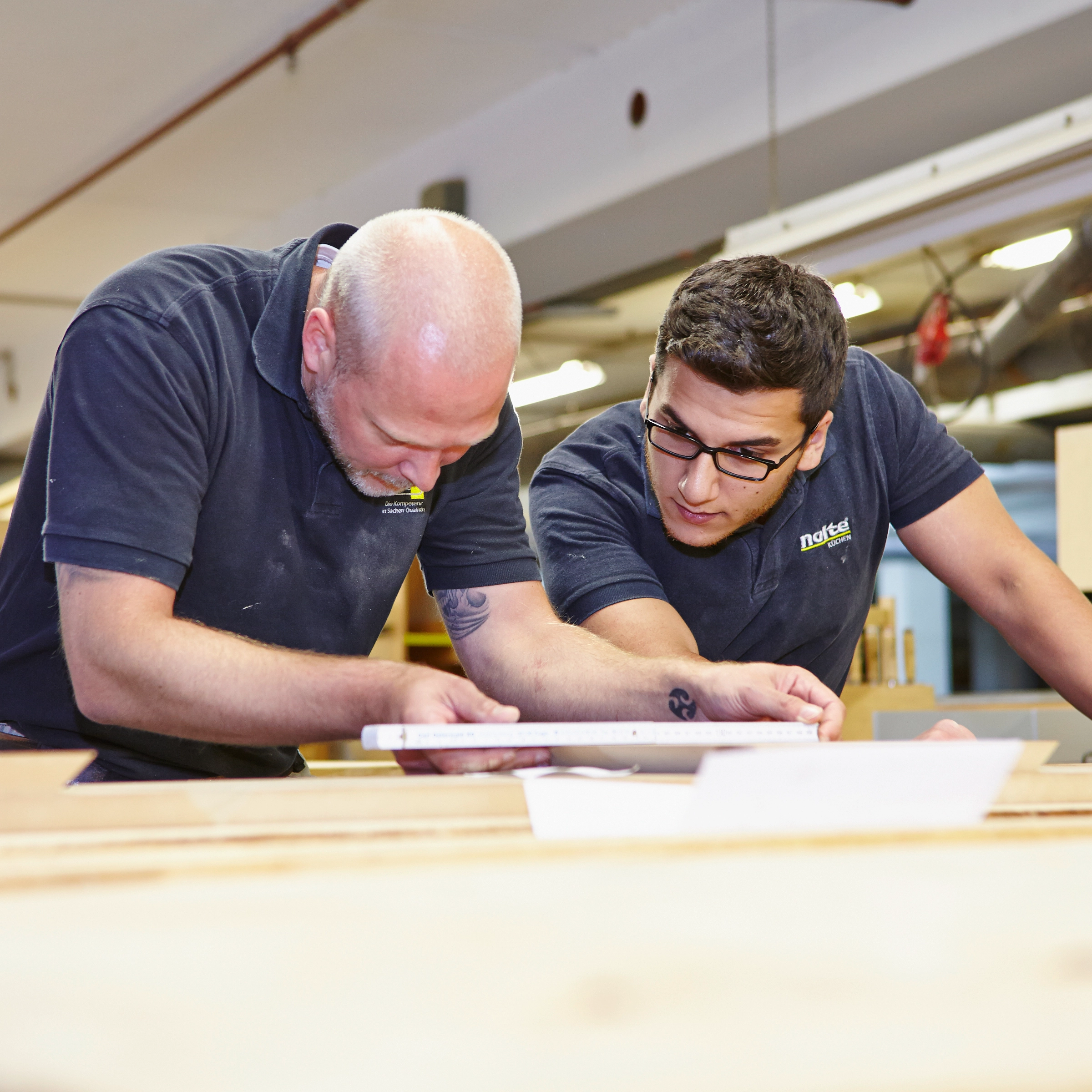 Zwei Männer arbeiten gemeinsam in einer Werkstatt an einem Holzprojekt für Nolte Küchen.