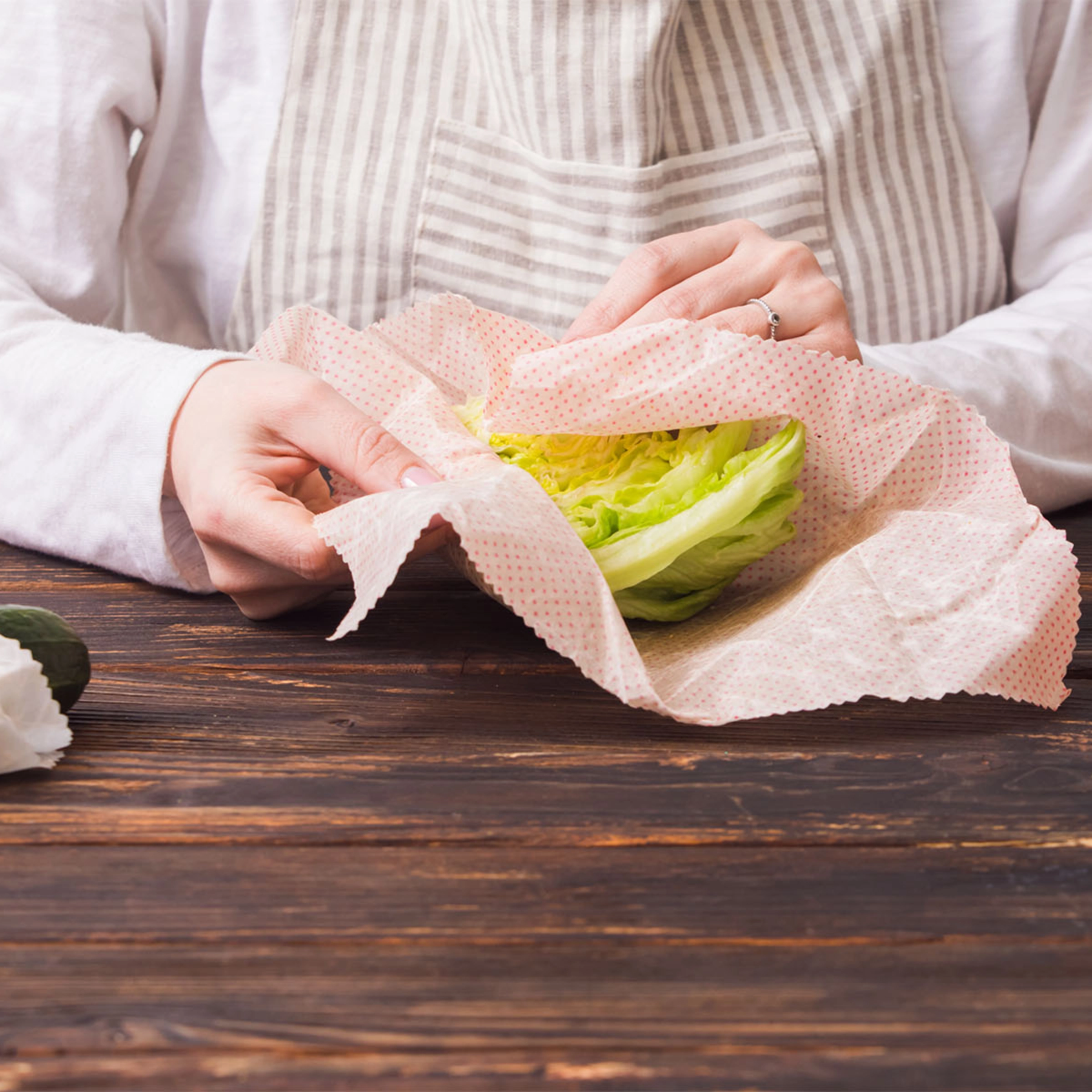 Une personne enveloppe de la salade dans des tissus de cire d'abeille sur une table en bois.