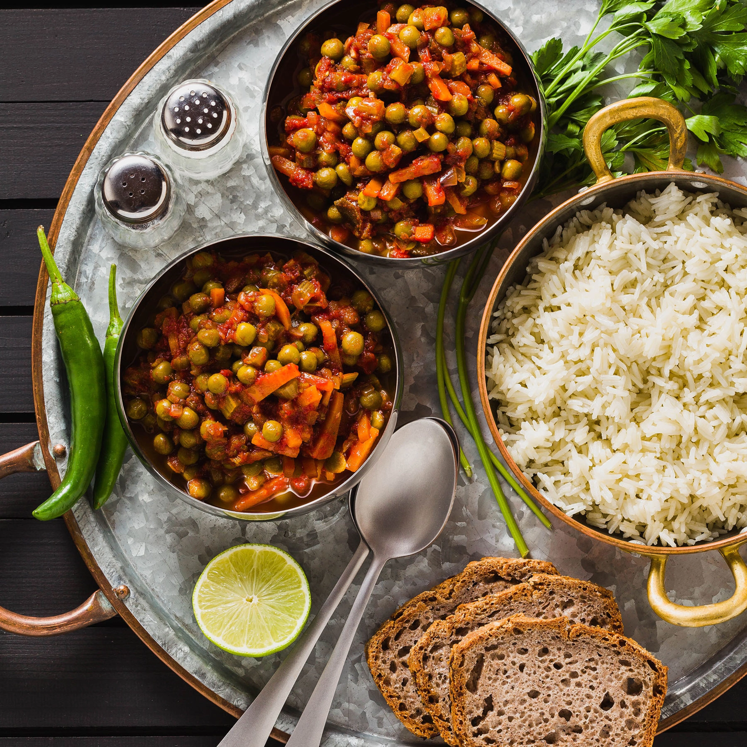 Un repas avec curry de pois, riz, pain, citron vert et épices, joliment présenté sur un plateau.
