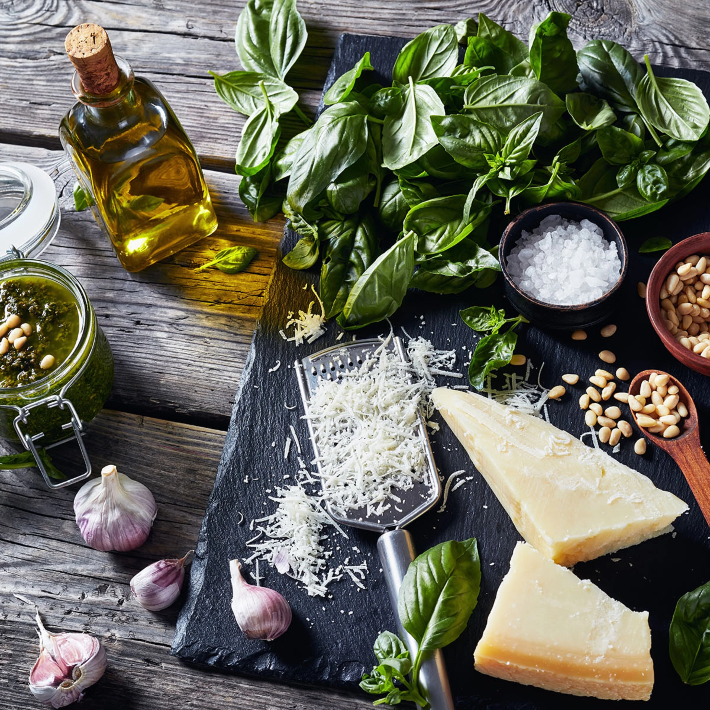 Sur une table en bois, des ingrédients pour le pesto, dont basilic, parmesan et ail.