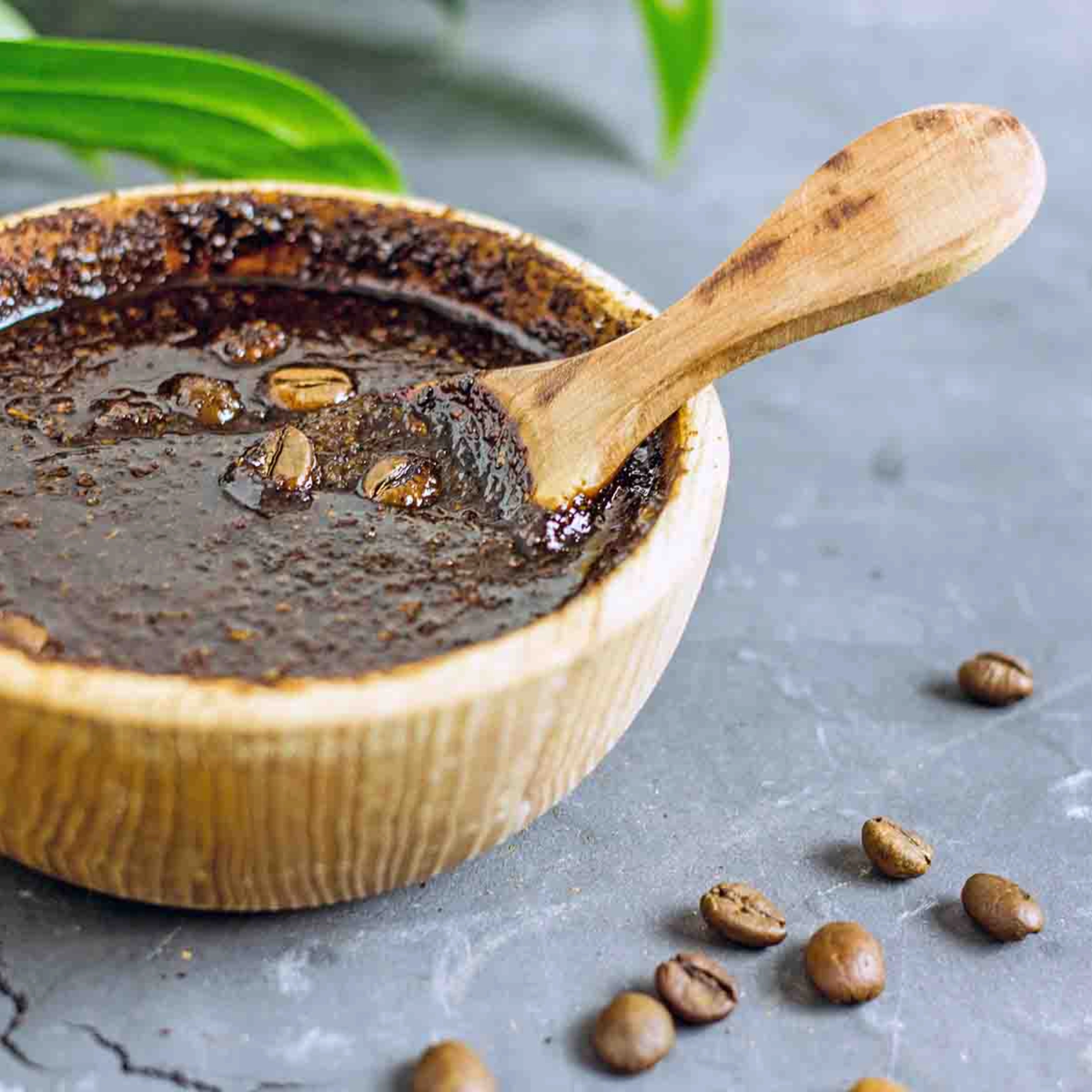Un bol avec un gommage au marc de café et des grains de café sur fond gris.