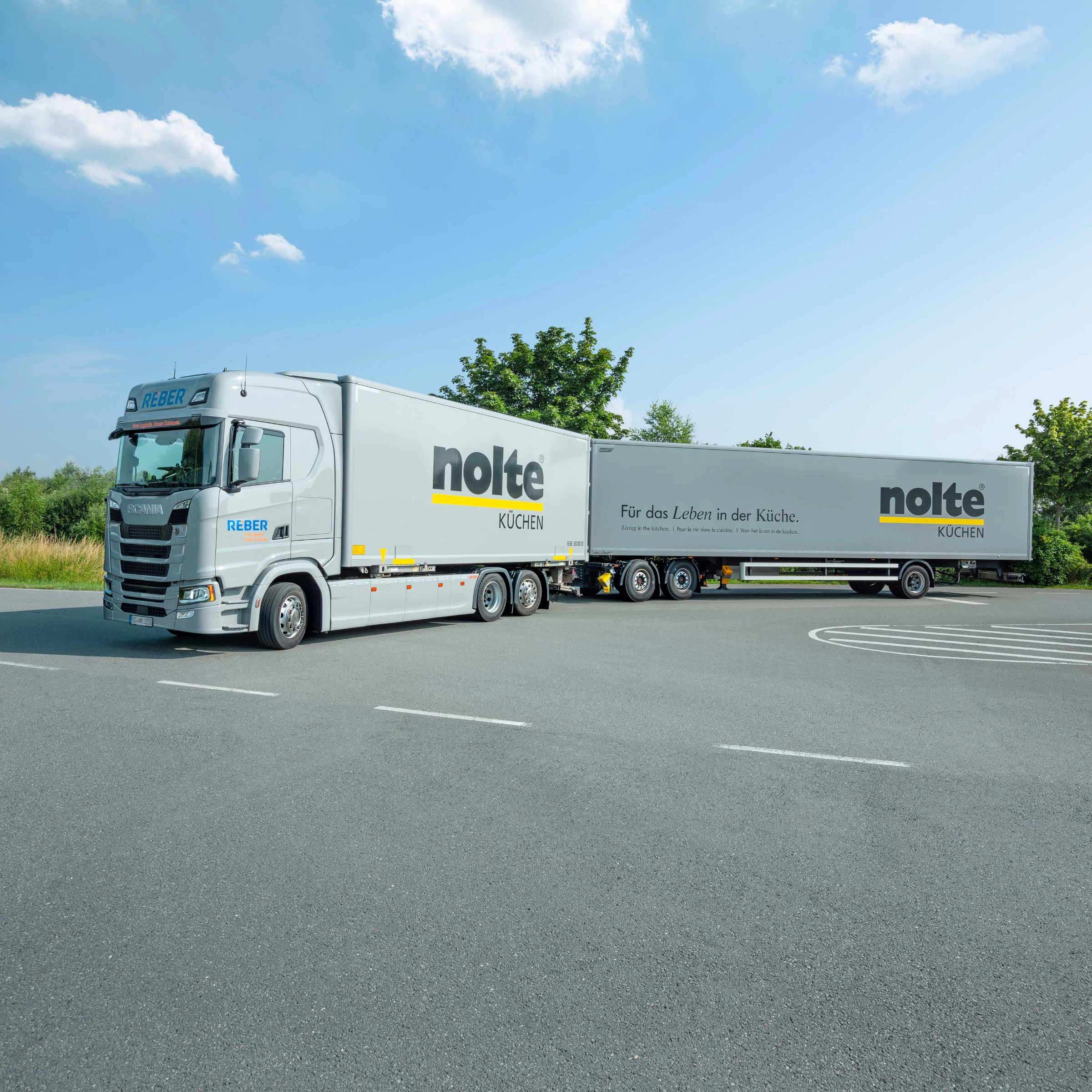 Un camion avec l'inscription "Nolte Kitchen" est garé sur un parking sous un ciel bleu.
