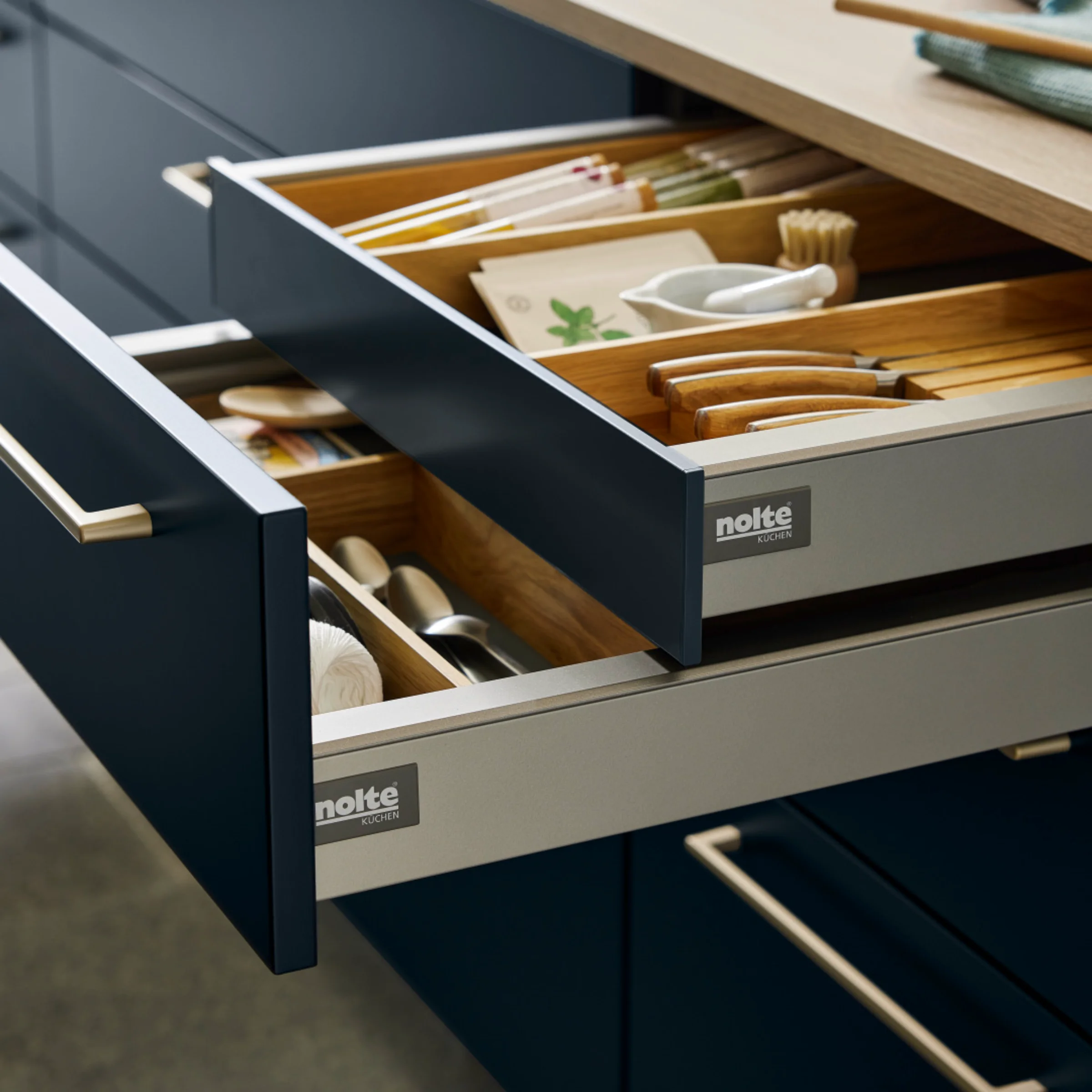 Eine moderne Küche mit geöffneten Schubladen von Nolte Küchen zeigt stilvolle Besteckorganisation.