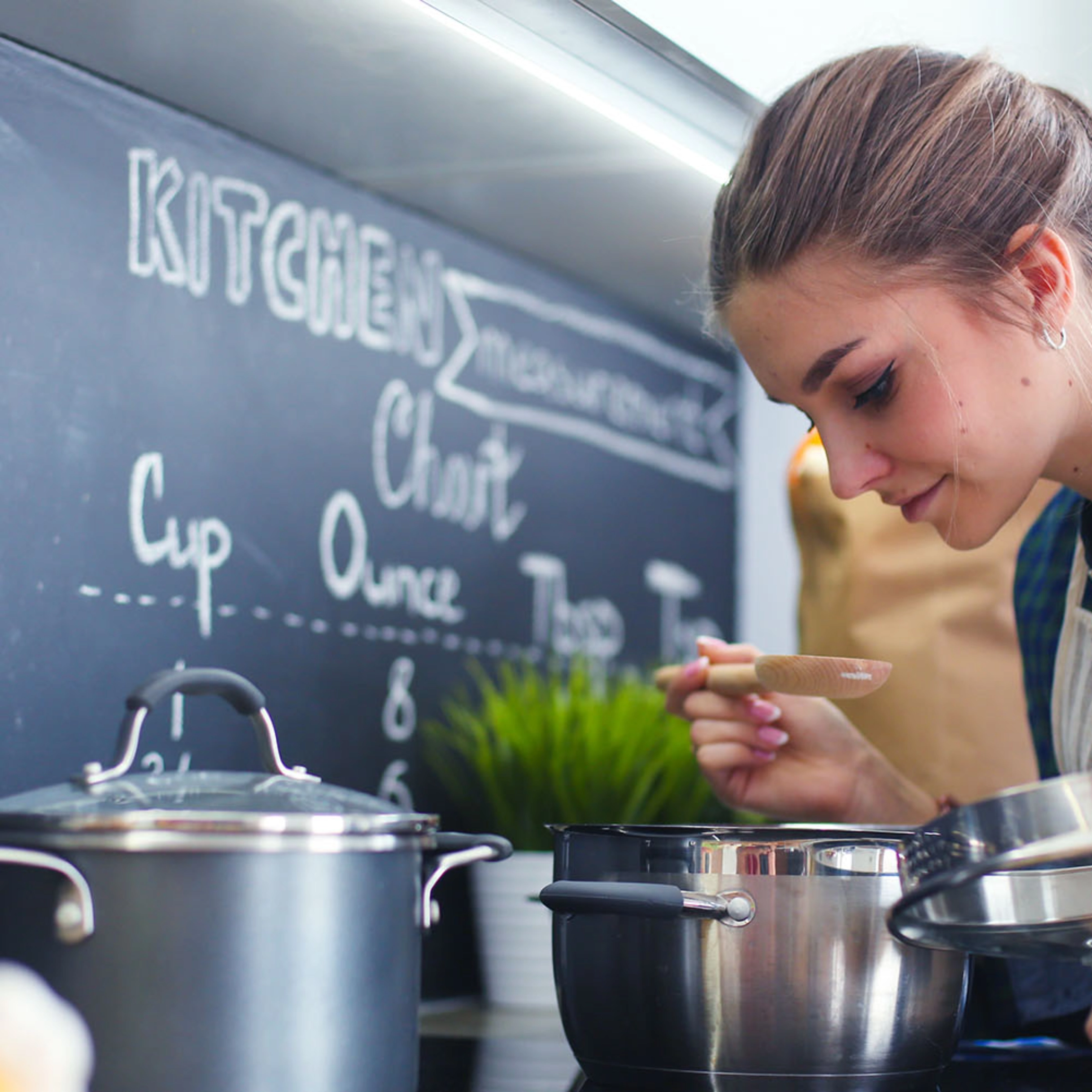 Une femme cuisine dans une cuisine moderne avec des casseroles et un tableau noir en arrière-plan, Nolte Kitchen.