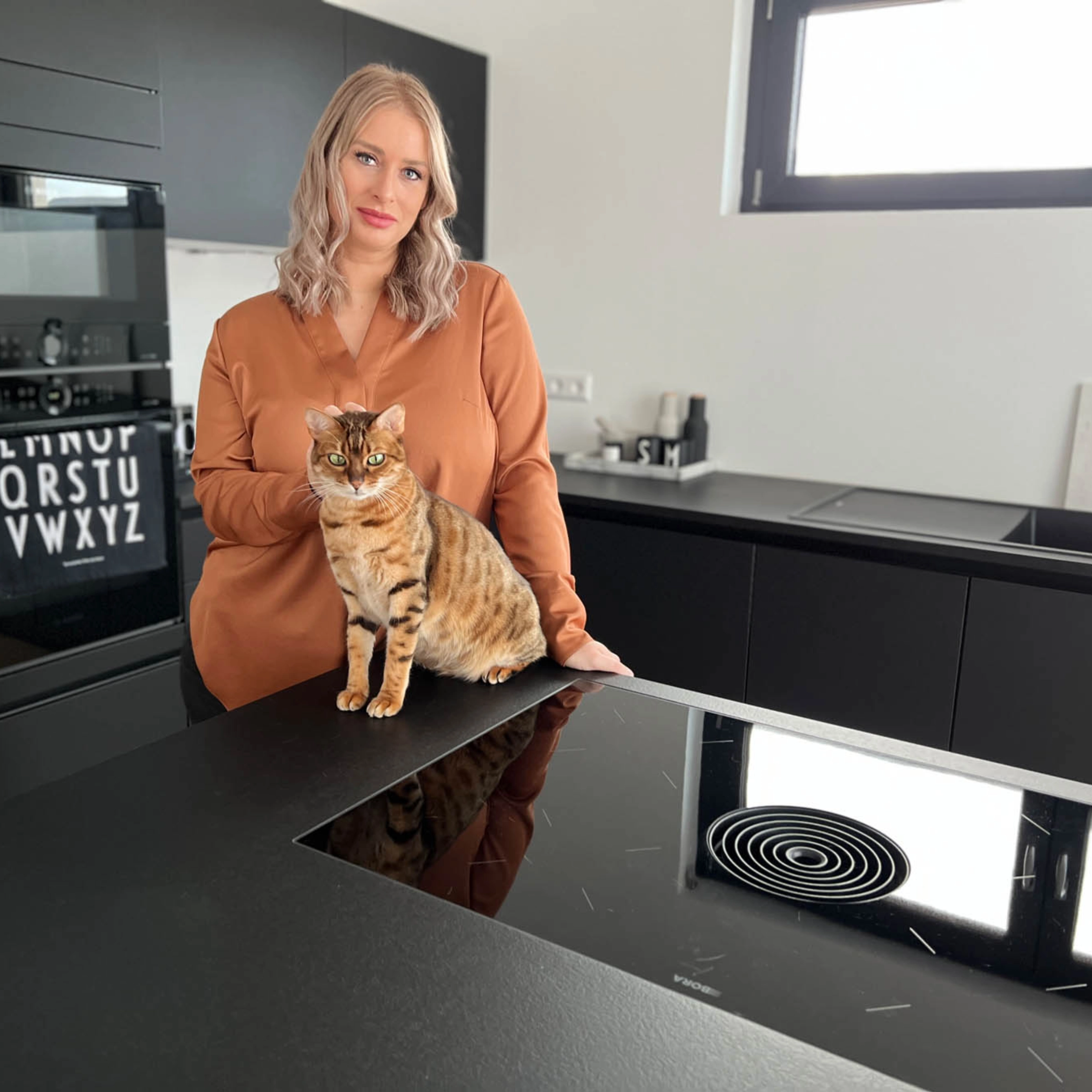 Una donna con un gatto in una cucina moderna con armadi neri. Nolte Kitchen.