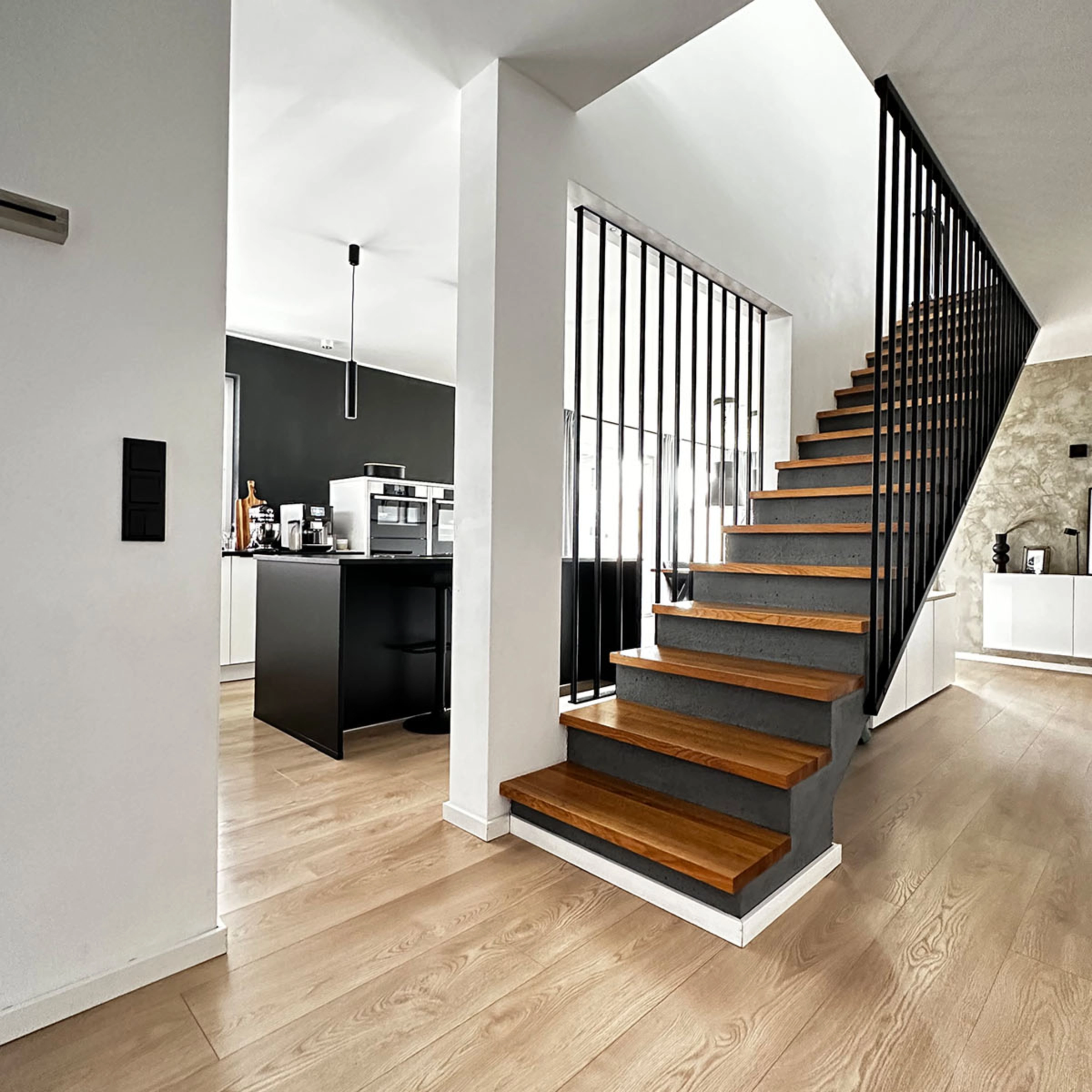 Cuisine moderne avec mur noir et îlot, escalier en bois à côté. Nolte Kitchen.