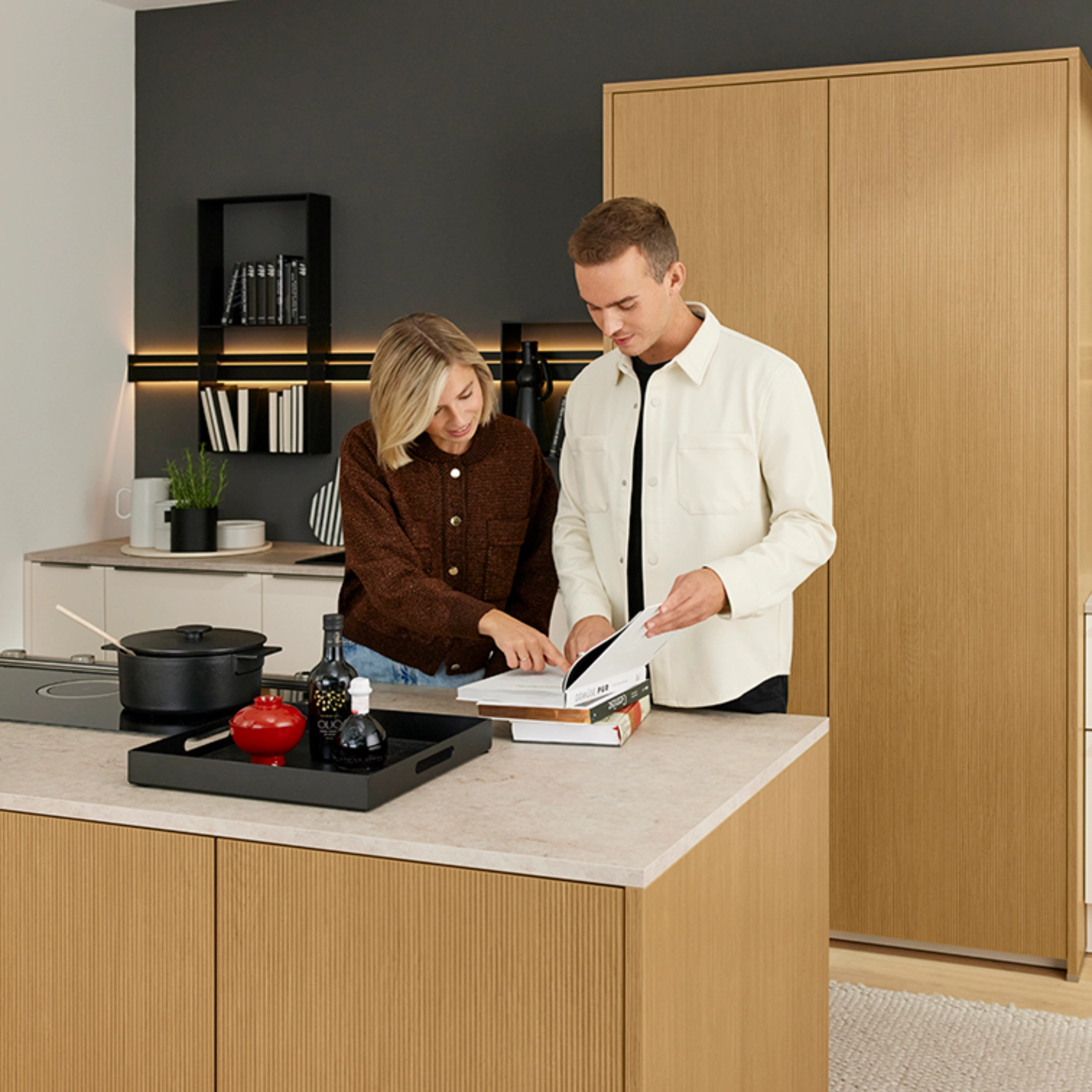 Un couple regarde un livre de cuisine dans une cuisine moderne avec des détails en bois, Nolte Kitchen.