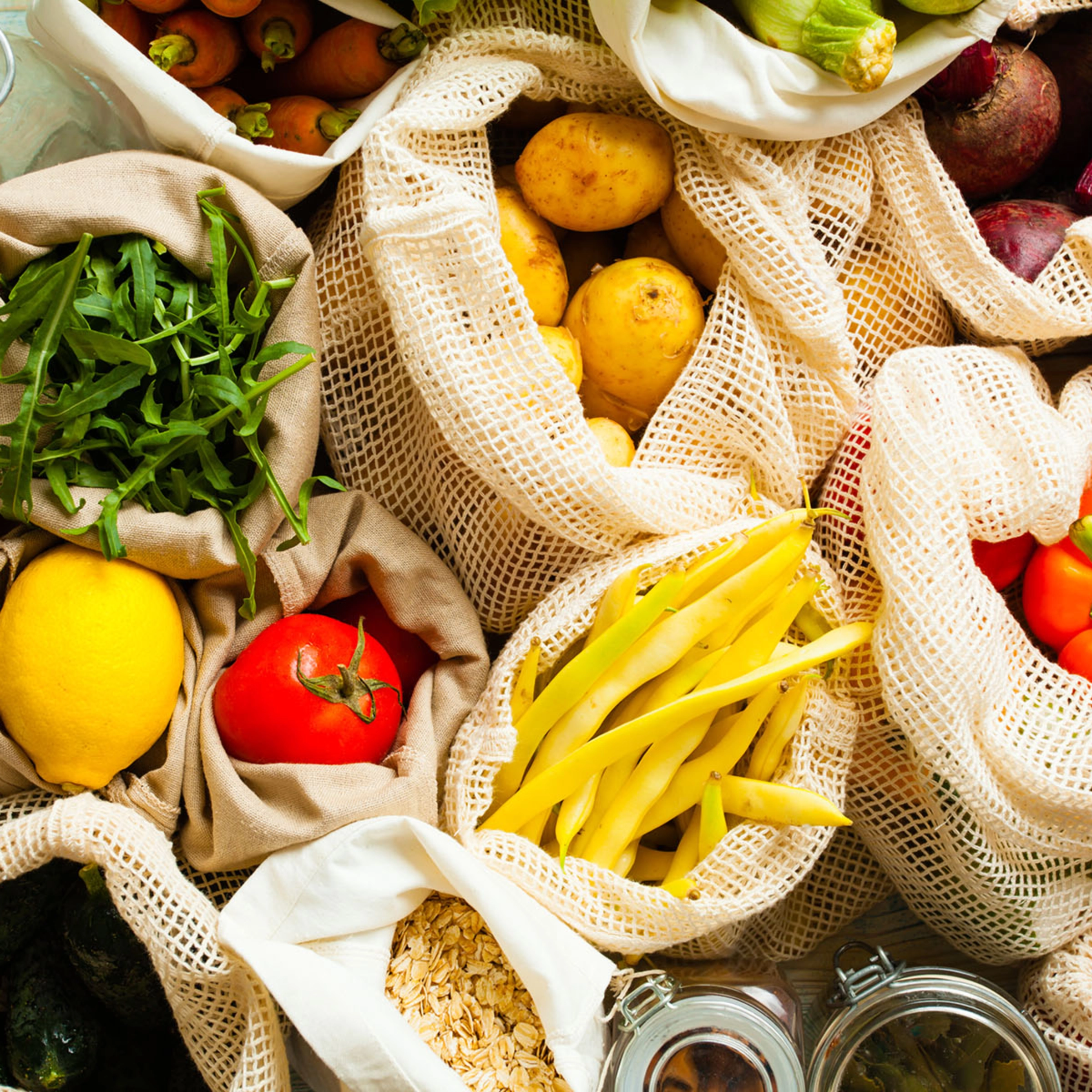 Divers légumes et fruits frais dans des sacs en tissu sur une table.