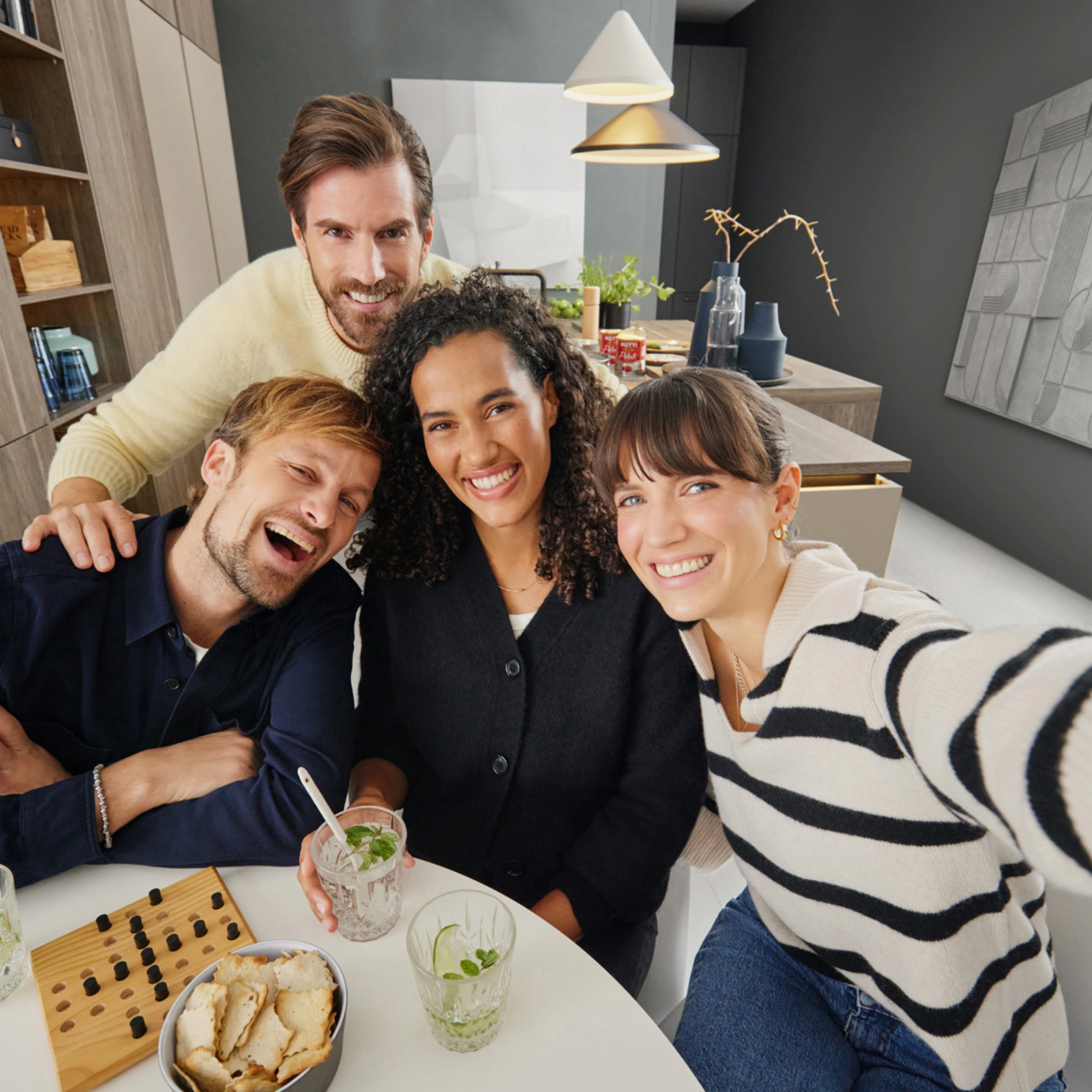 Eine Gruppe von Menschen sitzt lächelnd in einer modernen Küche. Nolte Küchen.