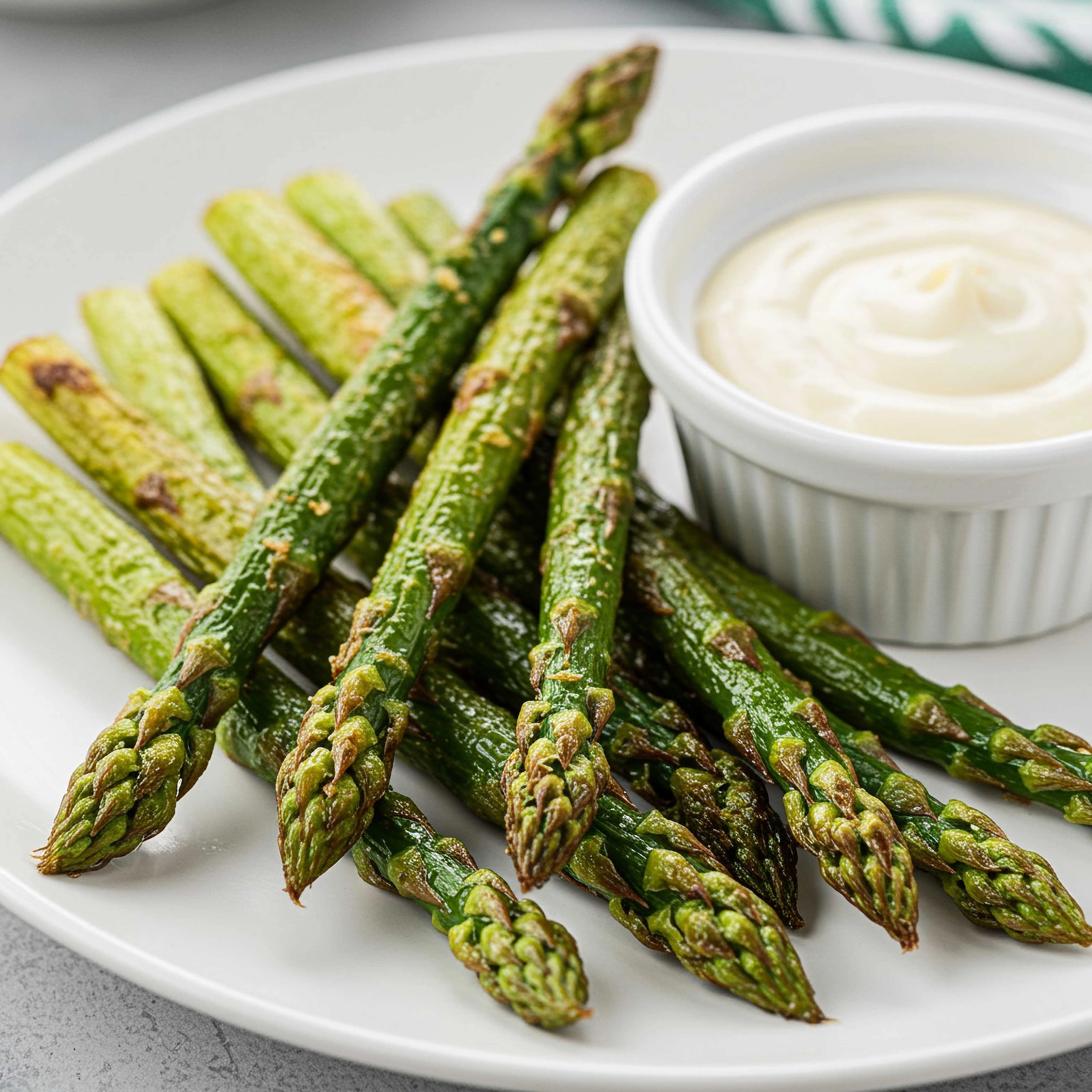 Green asparagus on a white plate with a bowl of dip.