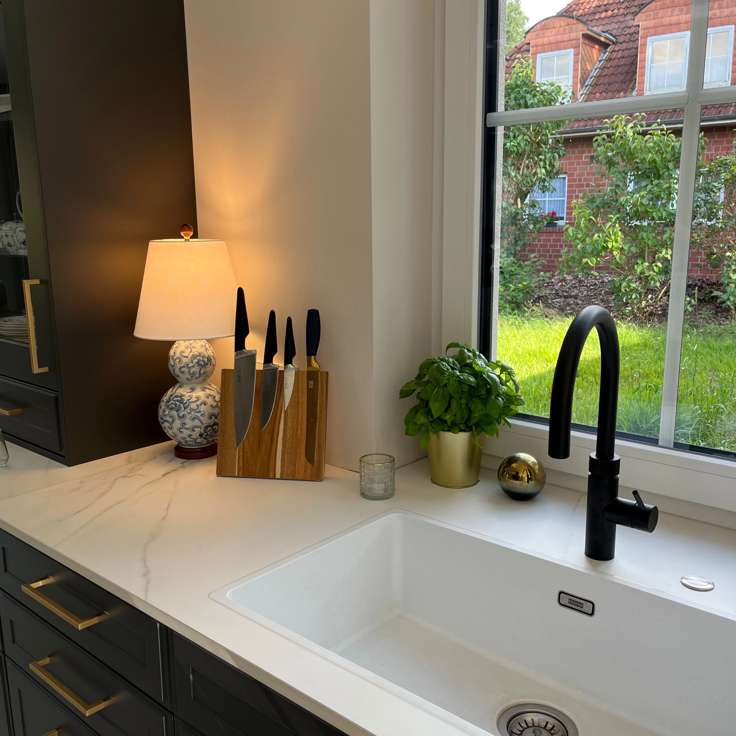 Dans une cuisine moderne avec évier blanc et pot d'herbes sur le plan de travail, conçue par Nolte Kitchen.
