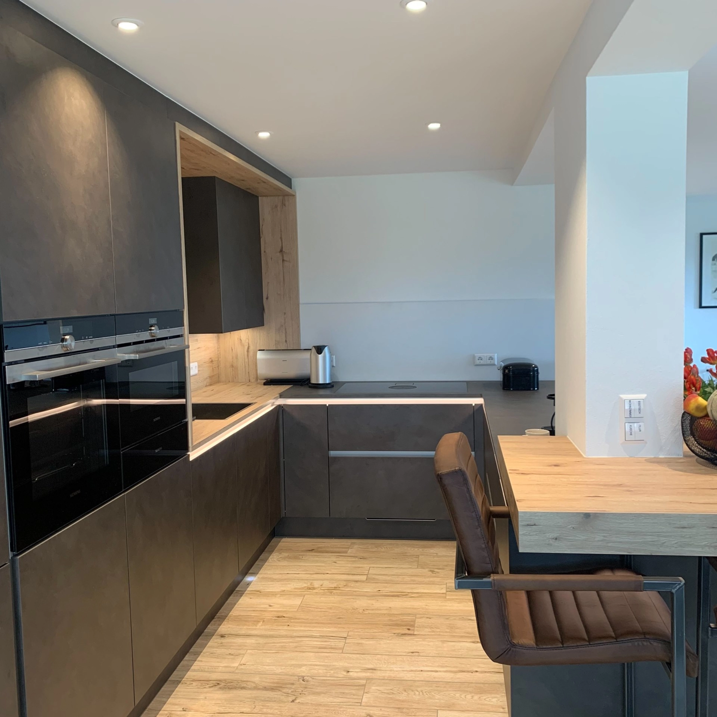 Cucina moderna con armadi scuri e accenti in legno, arredata da Nolte Kitchen.