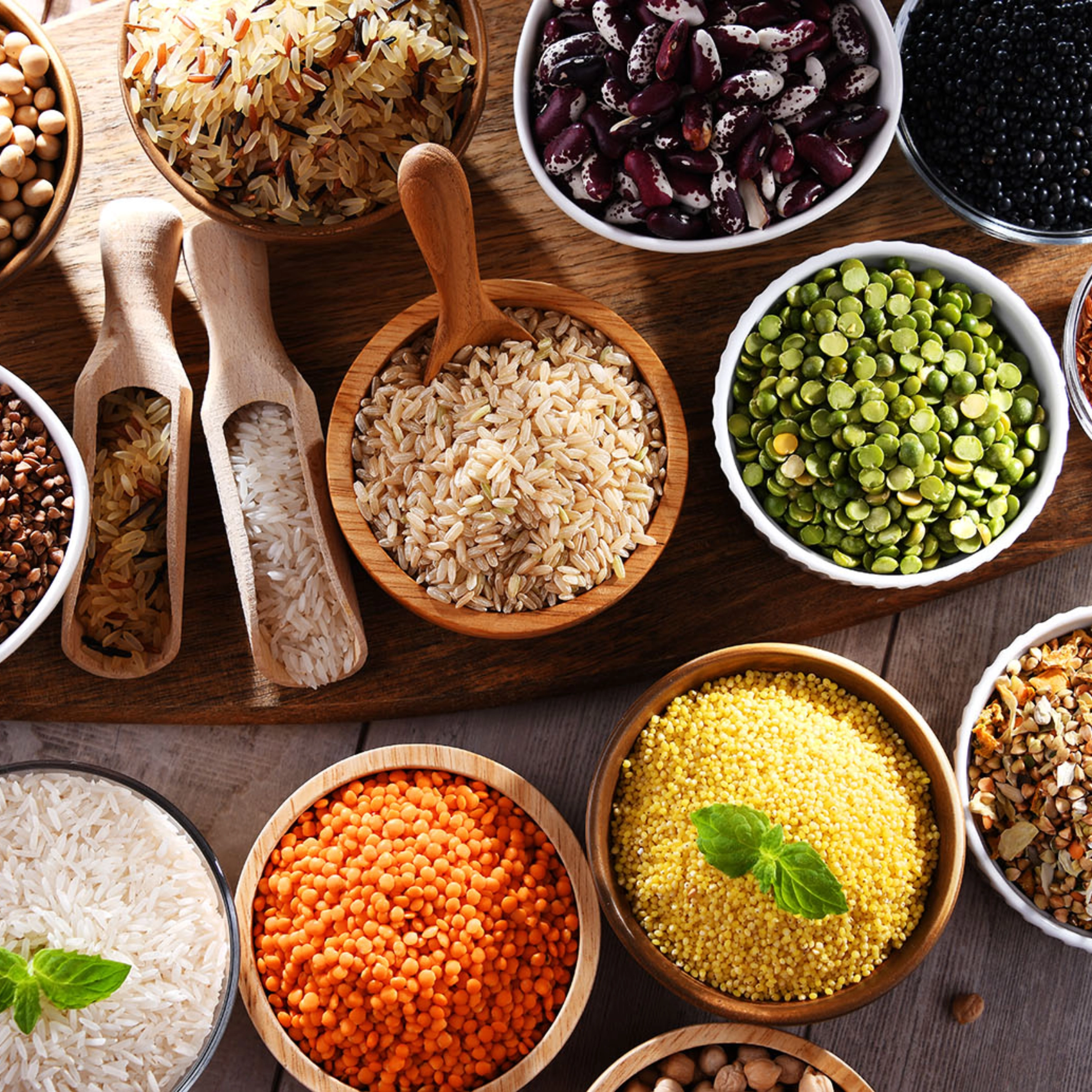 Divers bols de riz, lentilles et haricots disposés sur une table en bois.