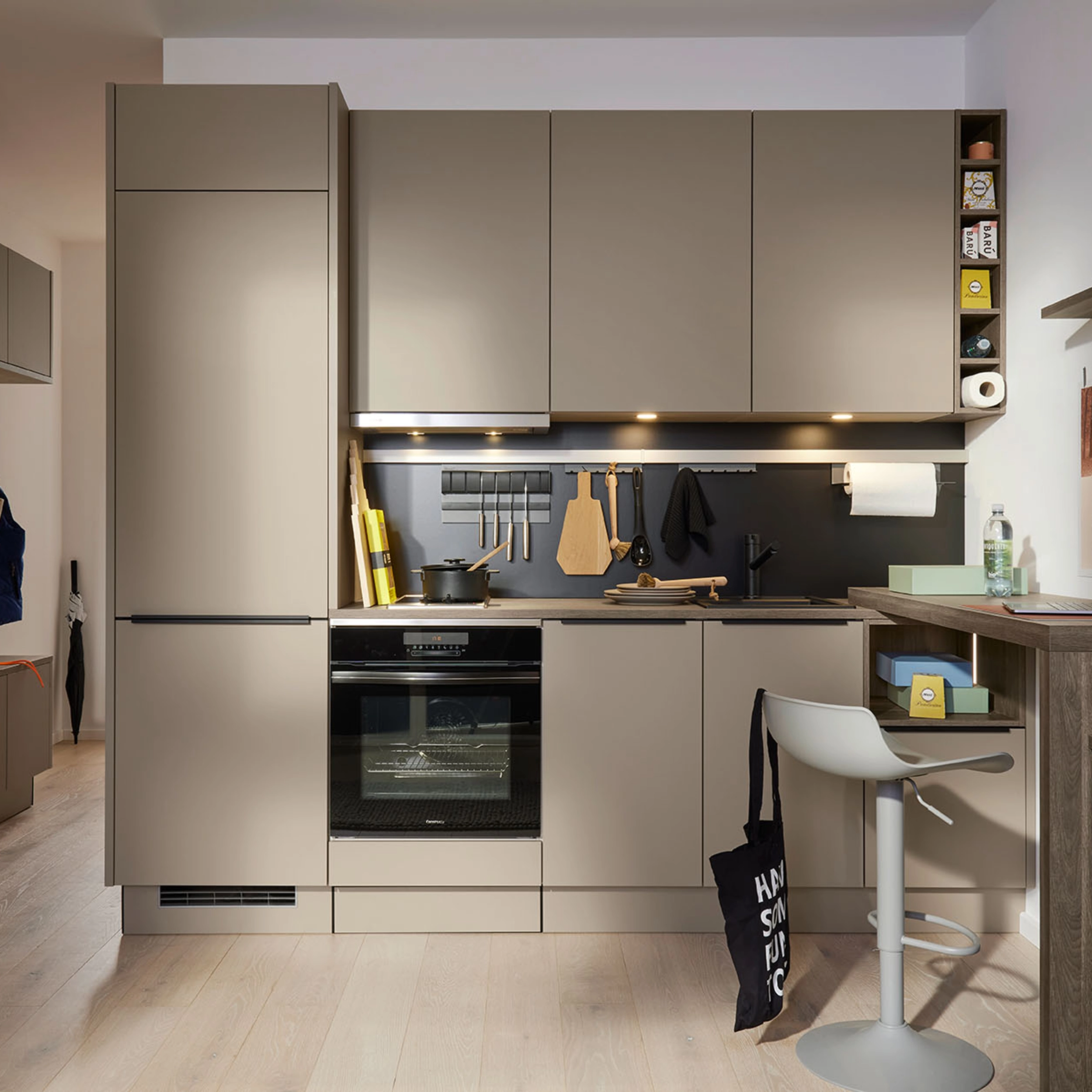 Moderne Küche mit beige Fronten und schwarzer Rückwand, ausgestattet mit Geräten und Dekor, Nolte Küchen.