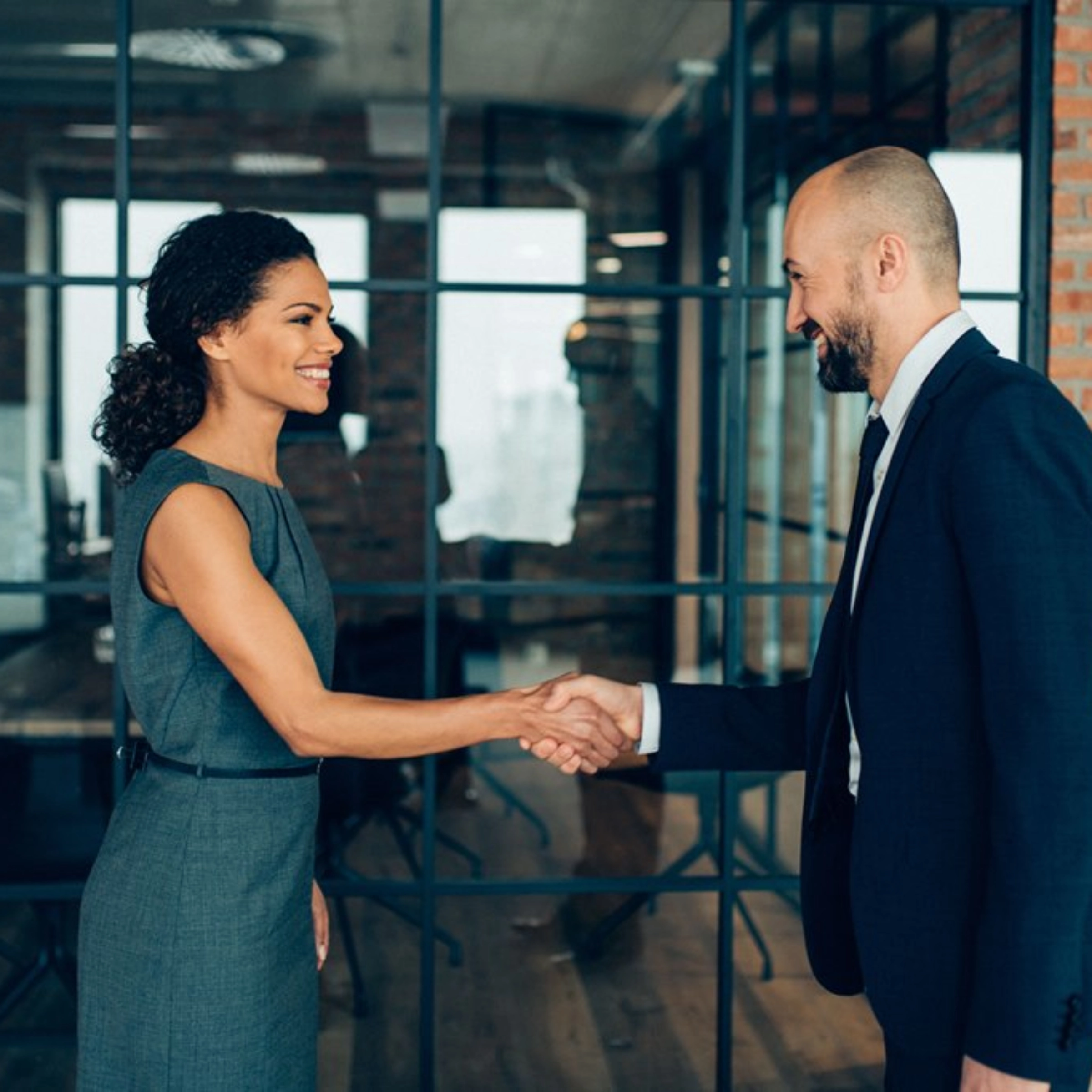 Two people in business attire shaking hands in a modern office.