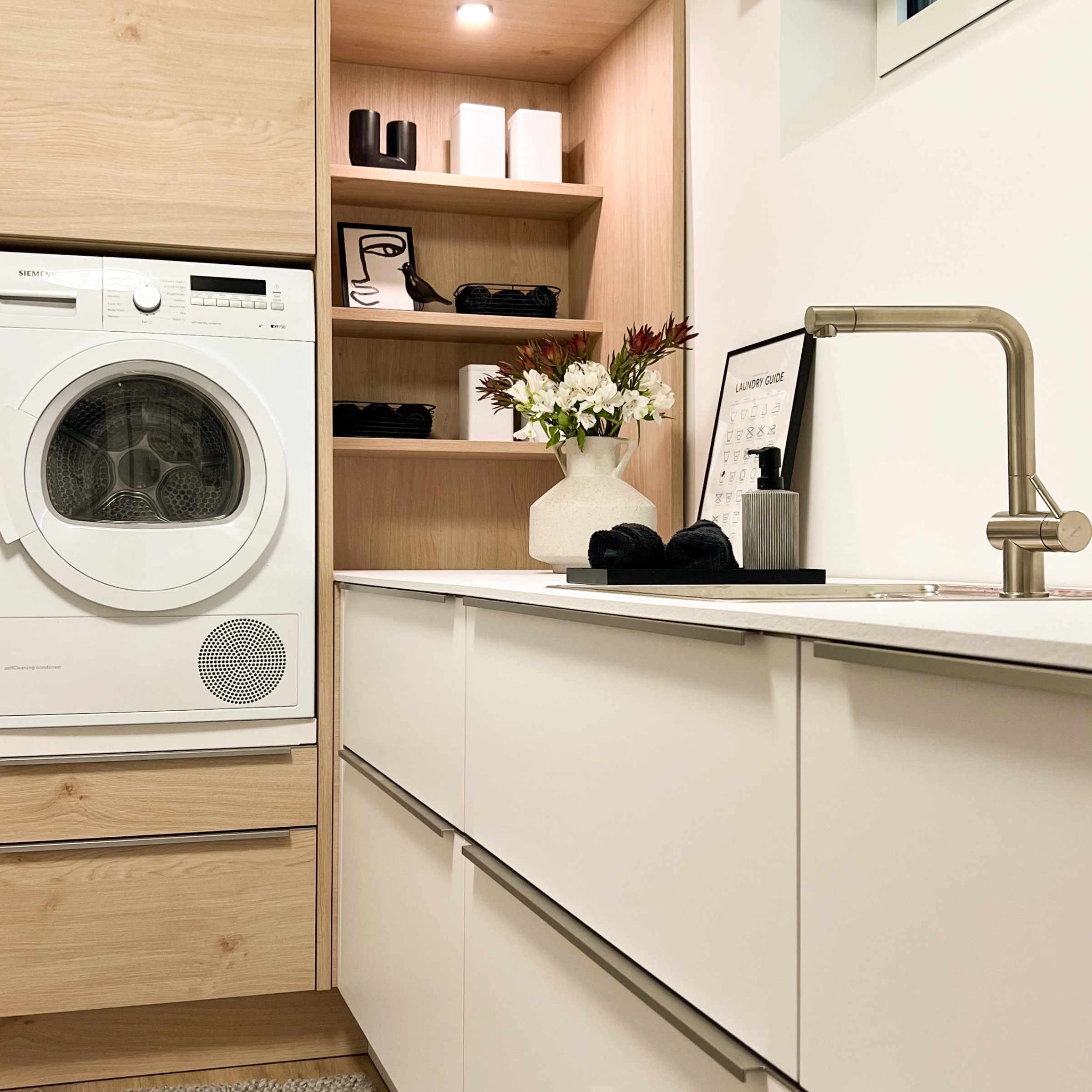 Un cuarto de lavado luminoso con lavadora y estantes, diseñado por Nolte Cuarto de Servicio.