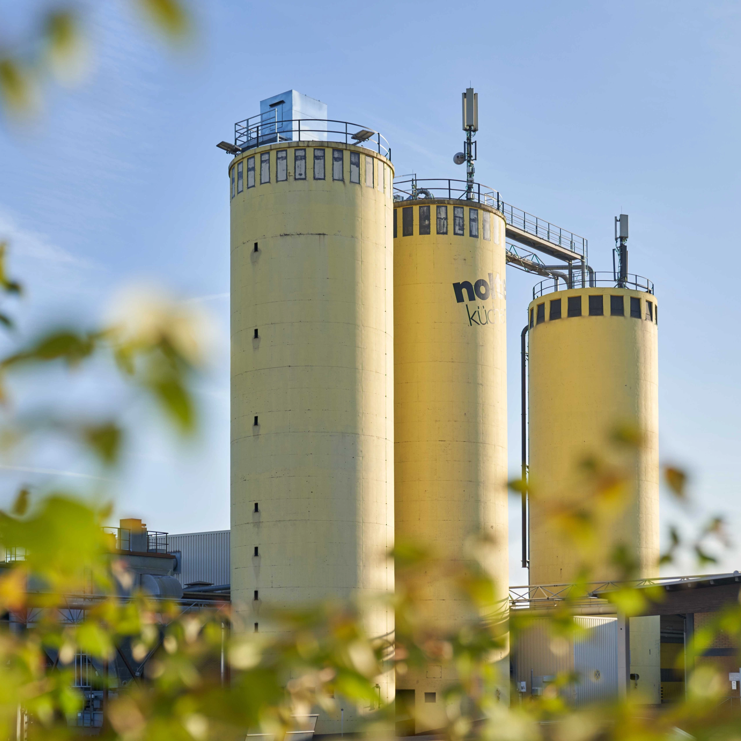 Trois grands silos jaunes avec l'inscription "Nolte Kitchen" devant un ciel dégagé.
