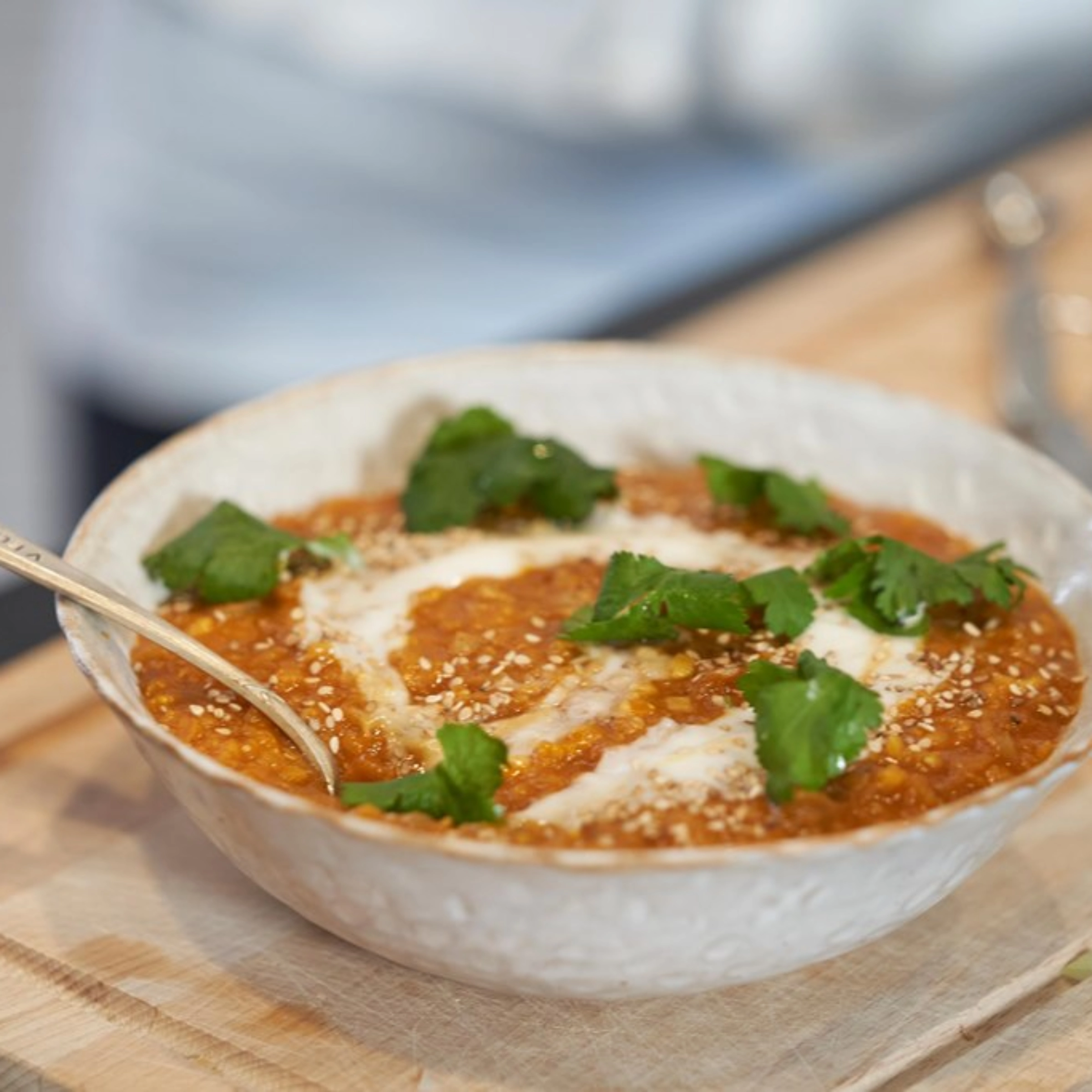 Eine Schüssel mit Linsensuppe, garniert mit Sahne und Koriander, steht auf einem Holzbrett.