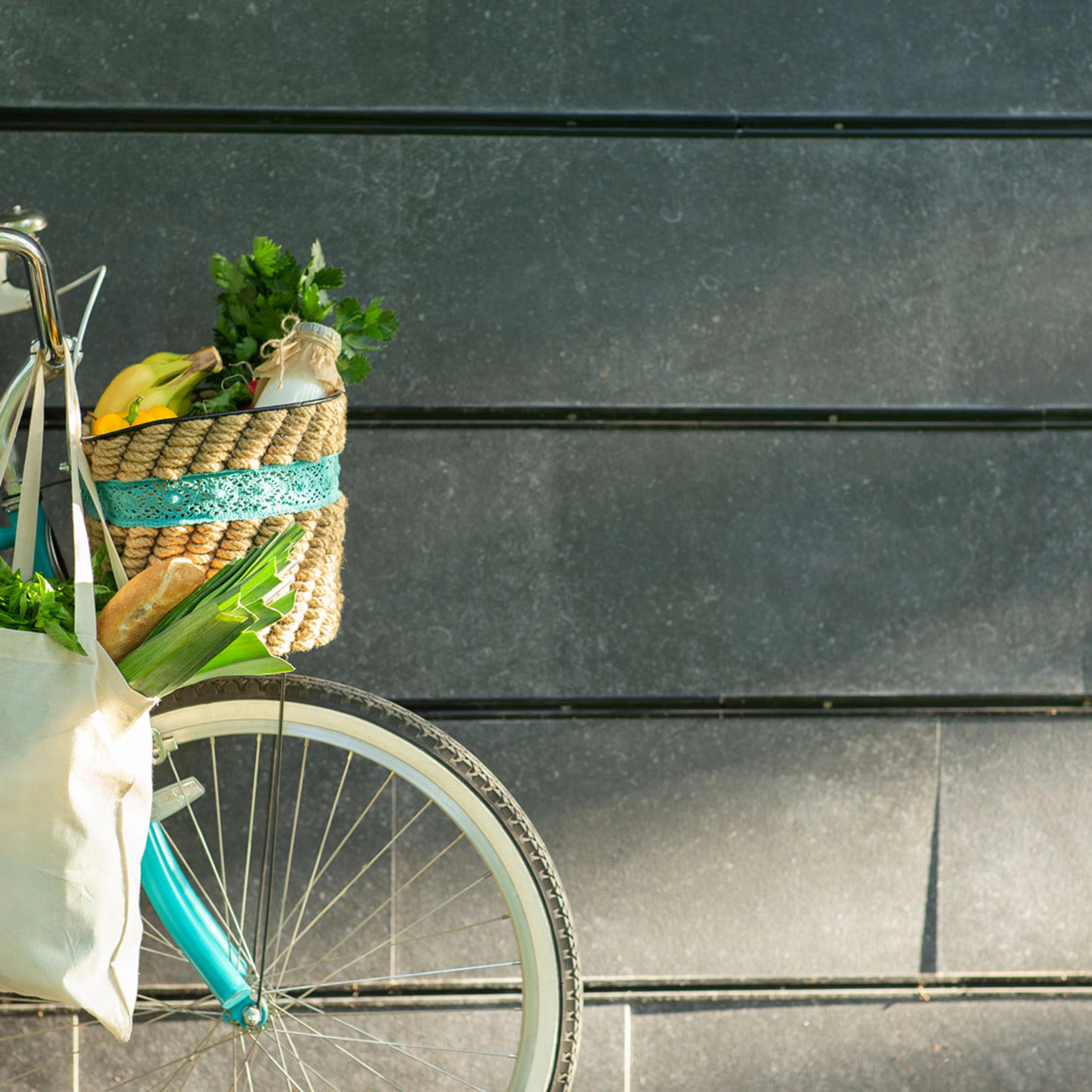 Un vélo avec un panier rempli de courses est appuyé contre un mur sombre.