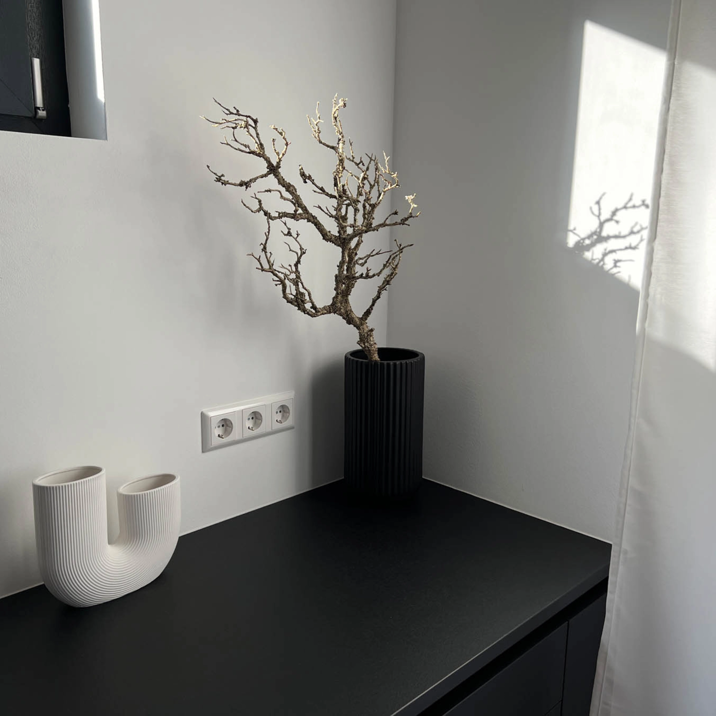 Su un piano di lavoro nero ci sono un vaso bianco e uno nero con un ramo, in stile Nolte Living.
