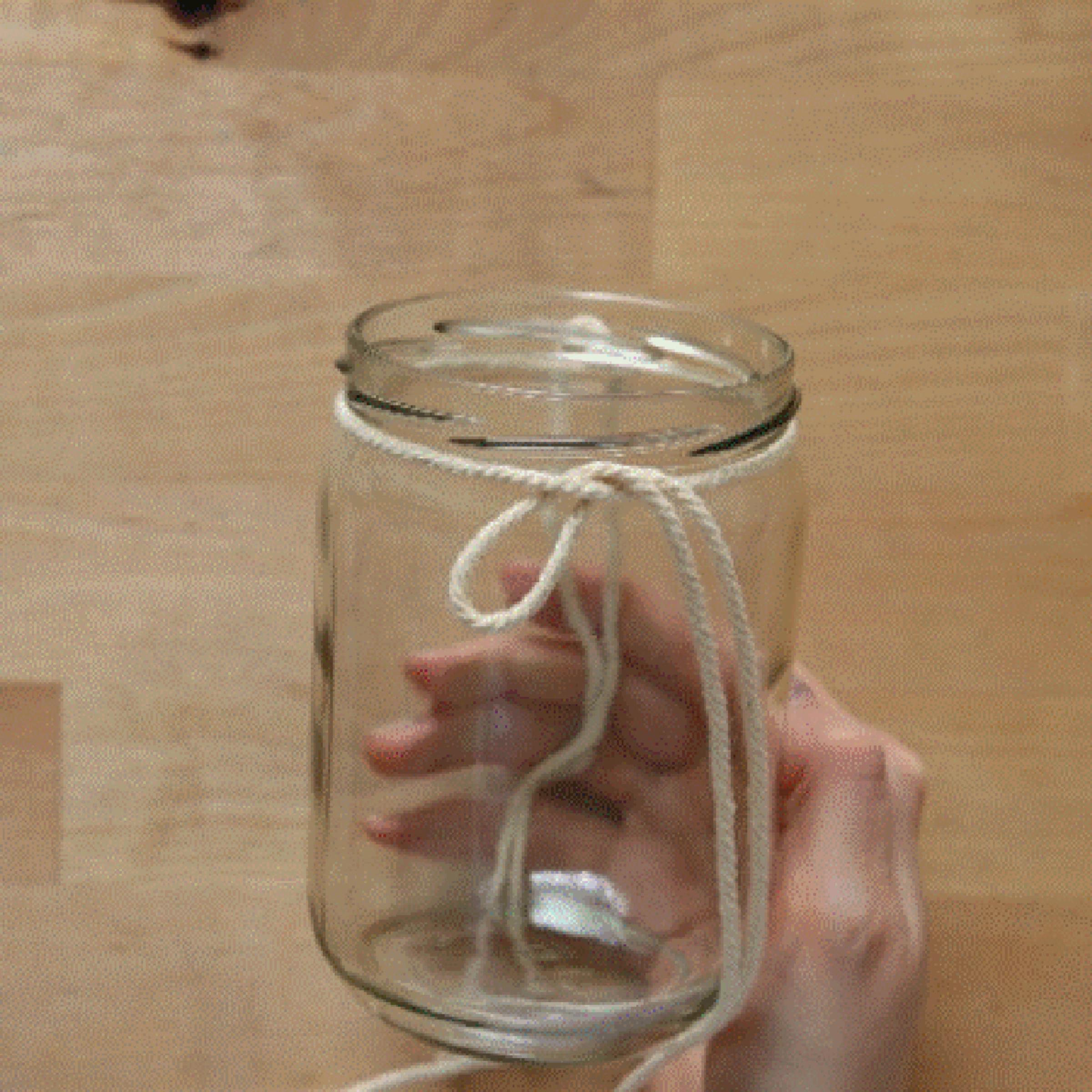 Une main tient un verre entouré d'une ficelle sur une table en bois.