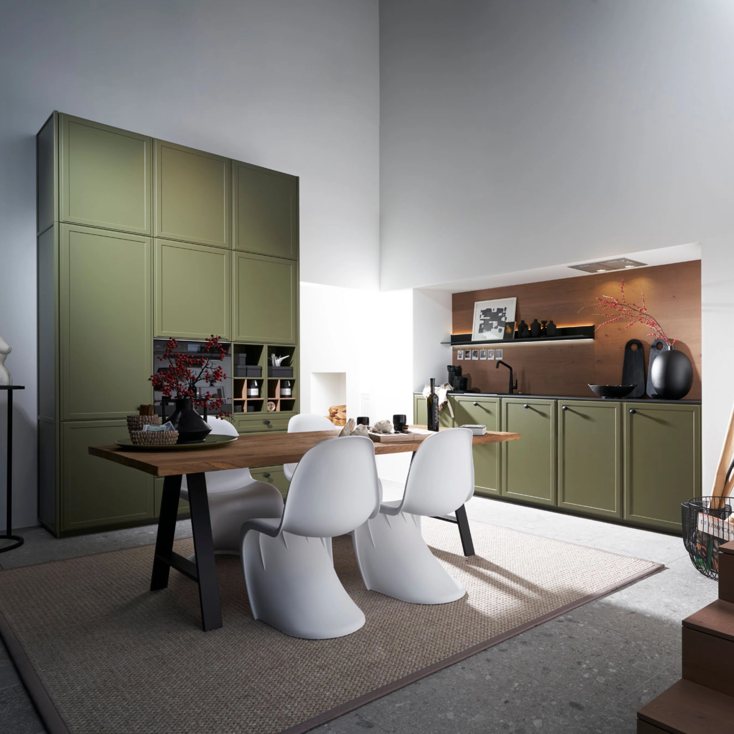 A modern kitchen with green cabinets and dining table, designed by Nolte Kitchen.