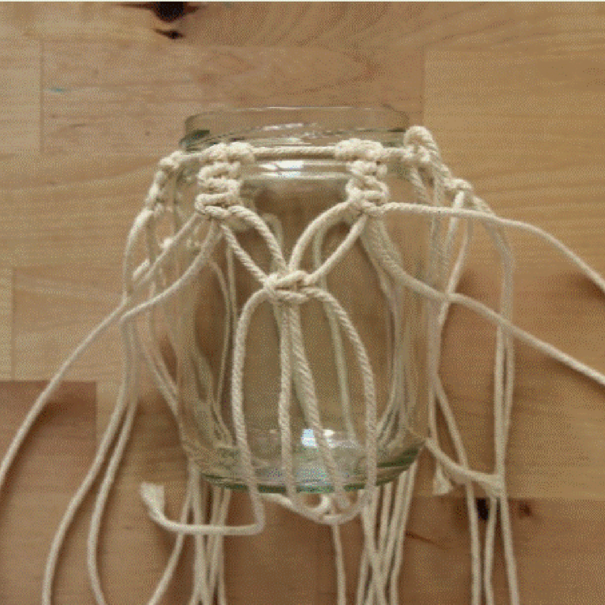 Un bocal avec support en macramé sur une table en bois.