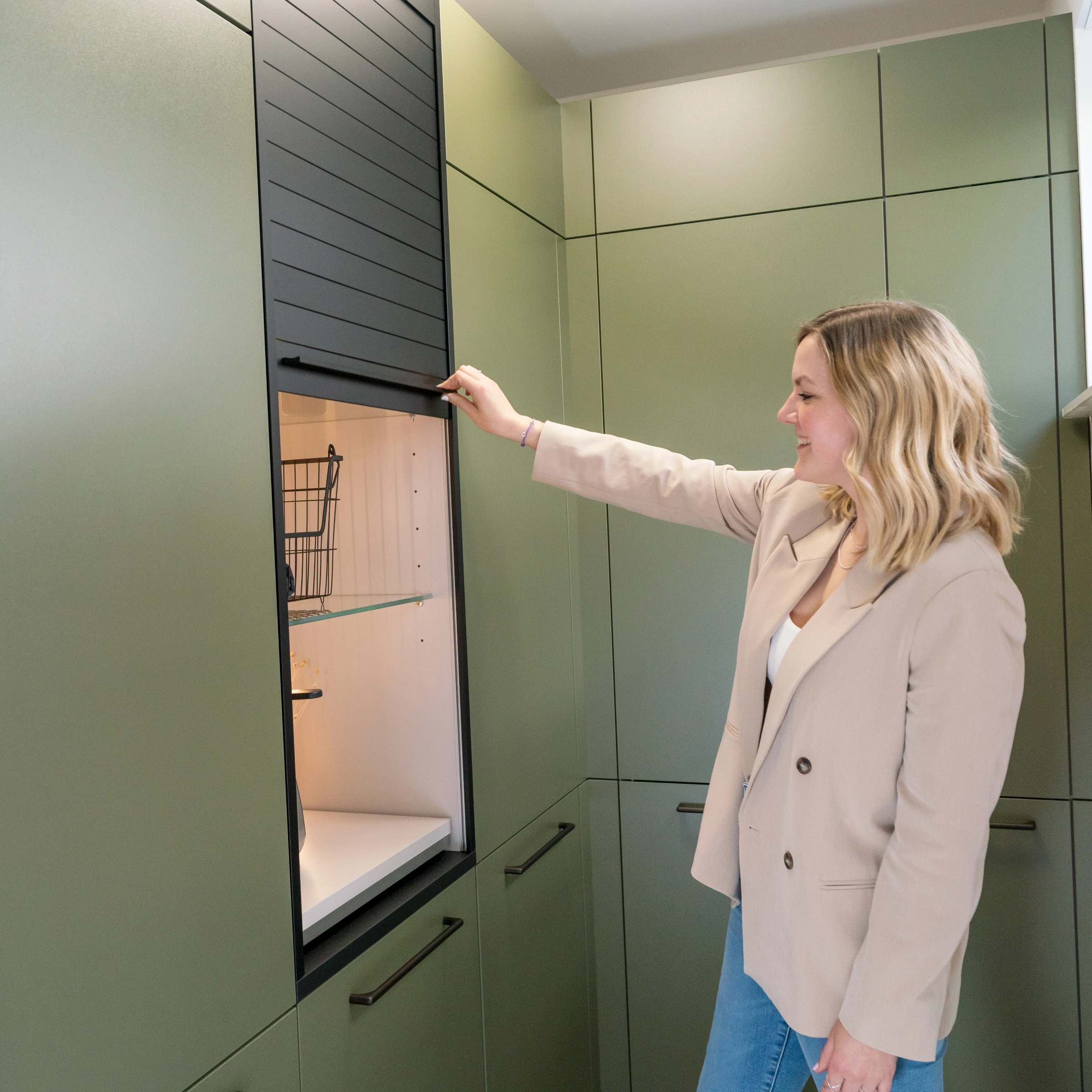 Une femme ouvre un placard dans une buanderie moderne conçue par Nolte Utility Rooms.