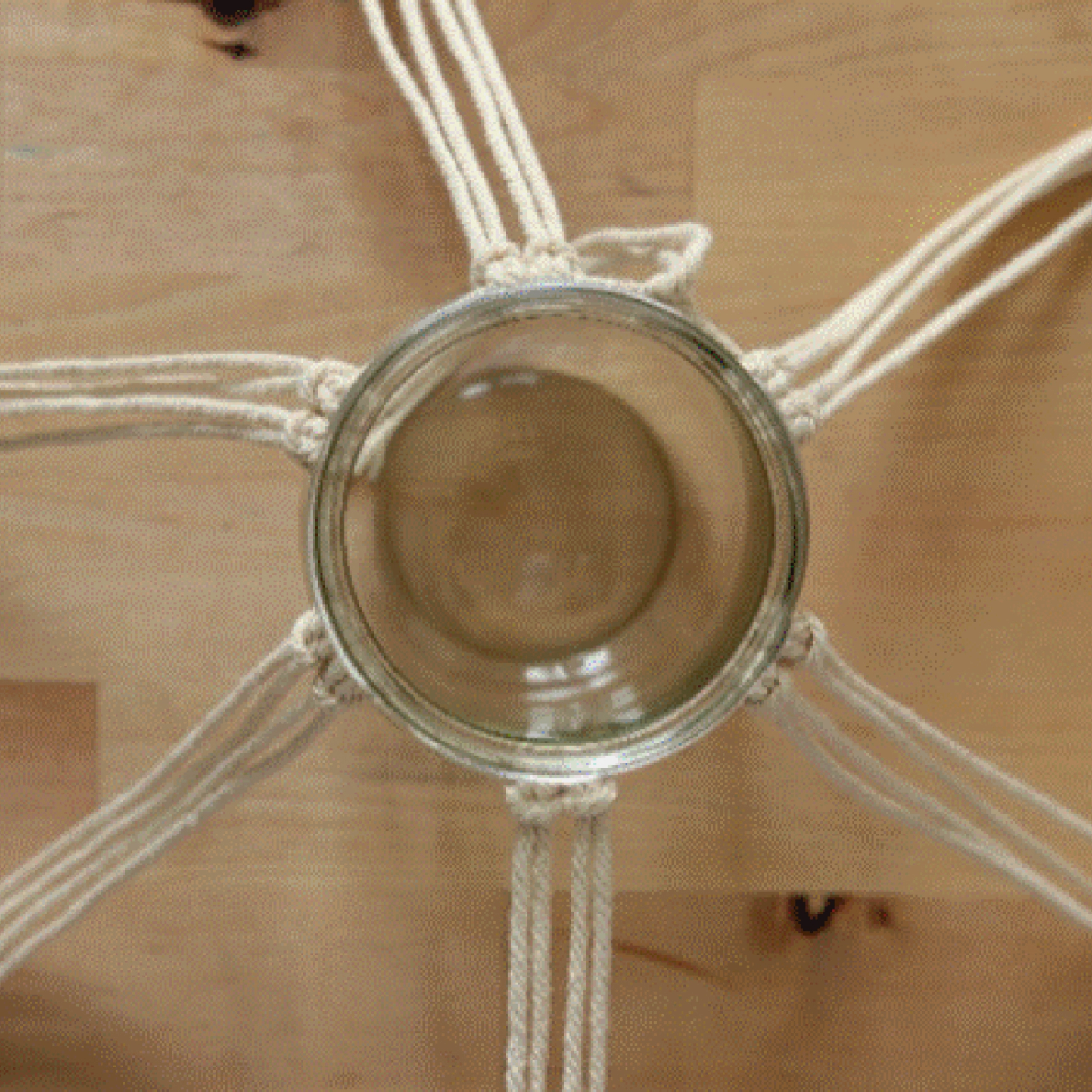 Un verre est maintenu par des cordes en macramé, étalées sur une table en bois.