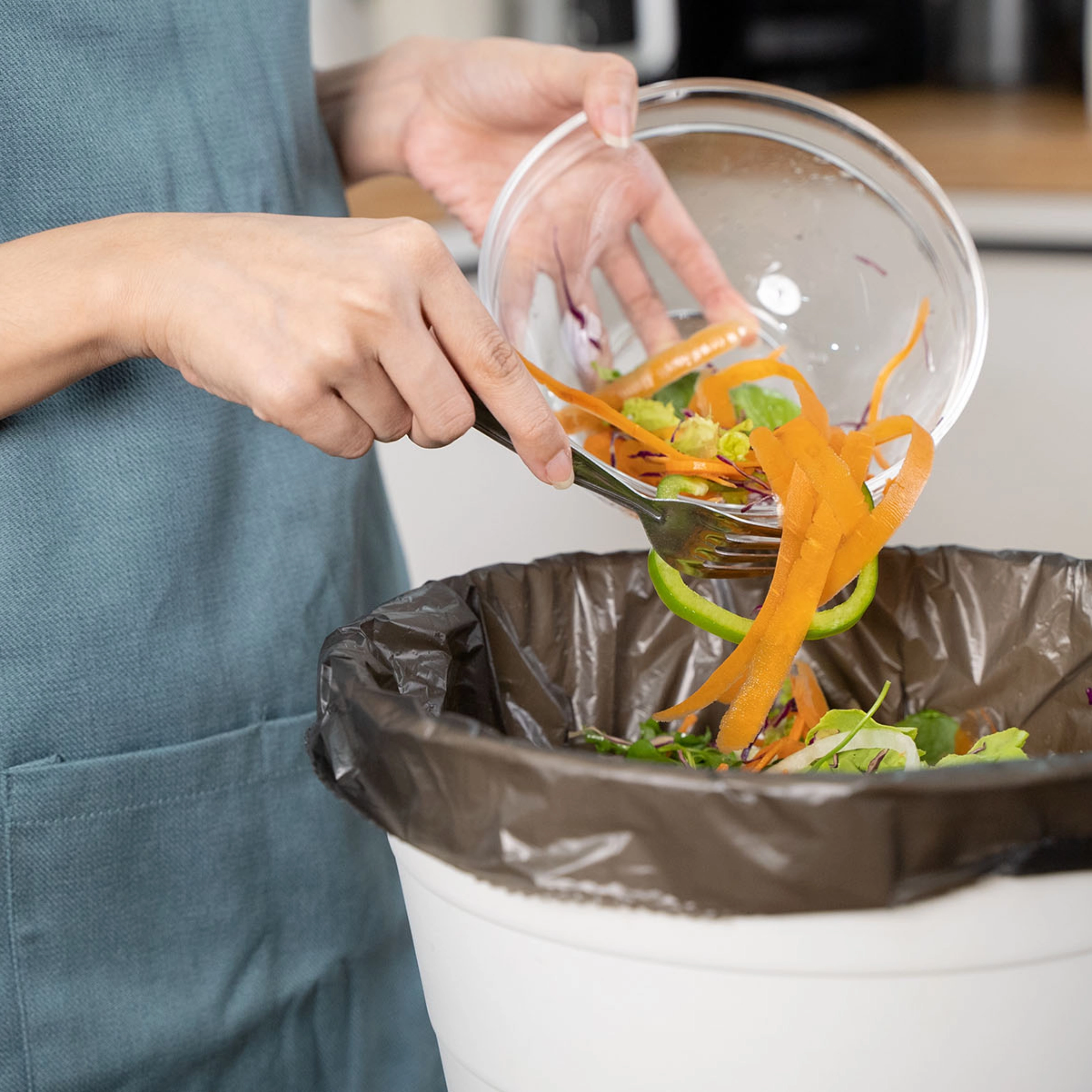 Une personne jette des restes de légumes dans une poubelle dans une cuisine moderne de Nolte Kitchen.