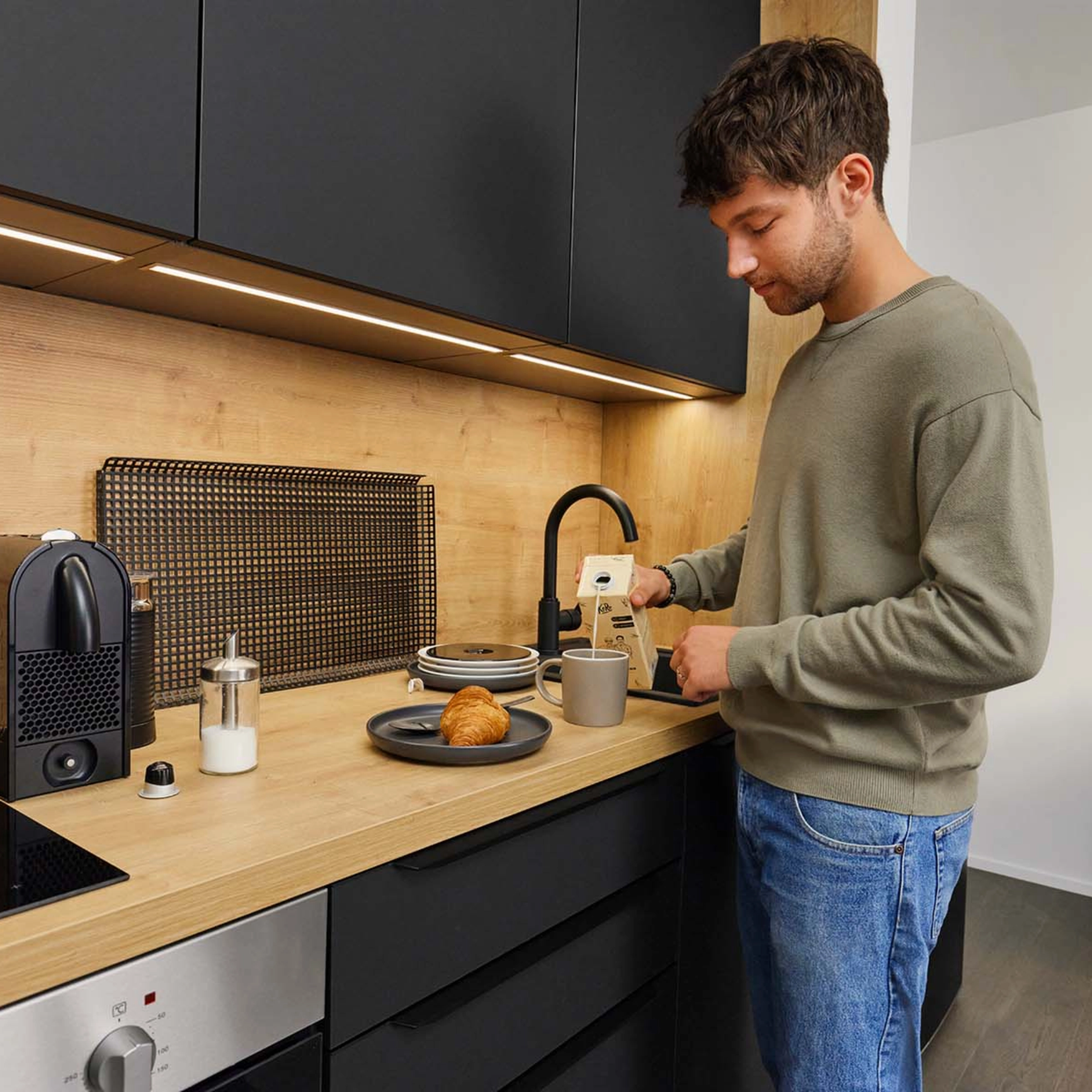 A man makes coffee in a modern kitchen with wood and black accents. Nolte Kitchens.