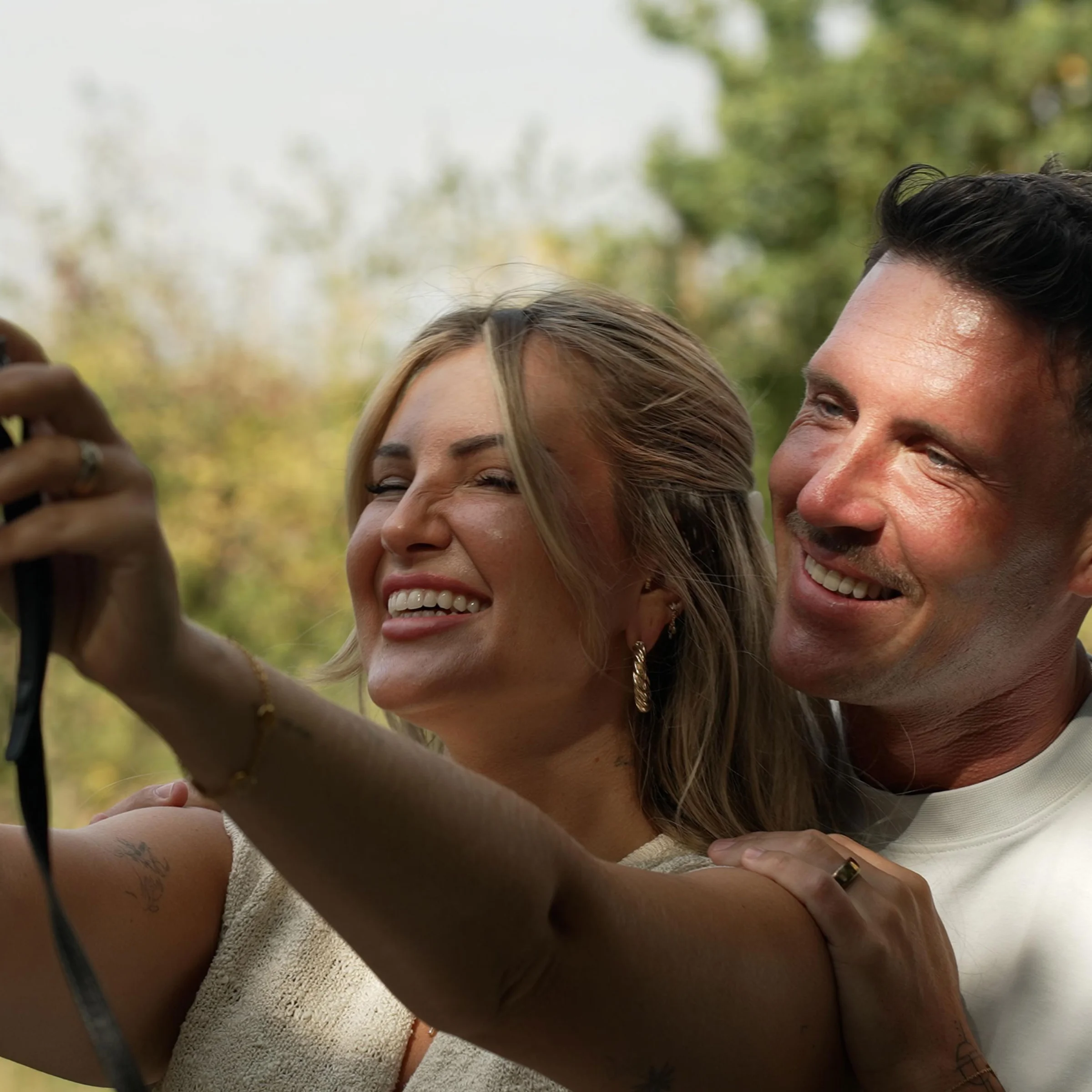 Un couple souriant prend un selfie dans un jardin ensoleillé.