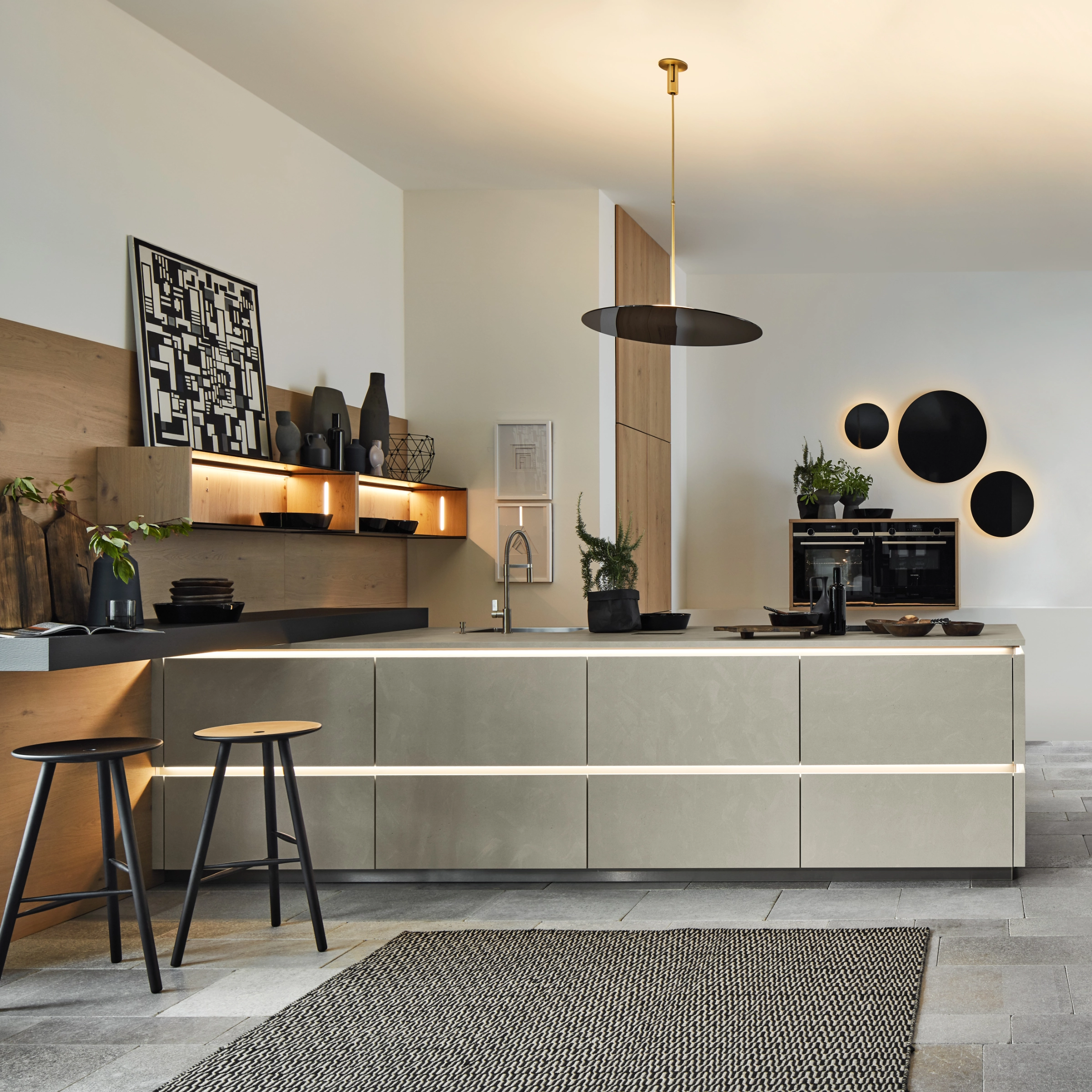 Eine moderne Küche mit Insel und Barhockern, dekoriert mit Pflanzen und Kunstwerken. Nolte Küchen.