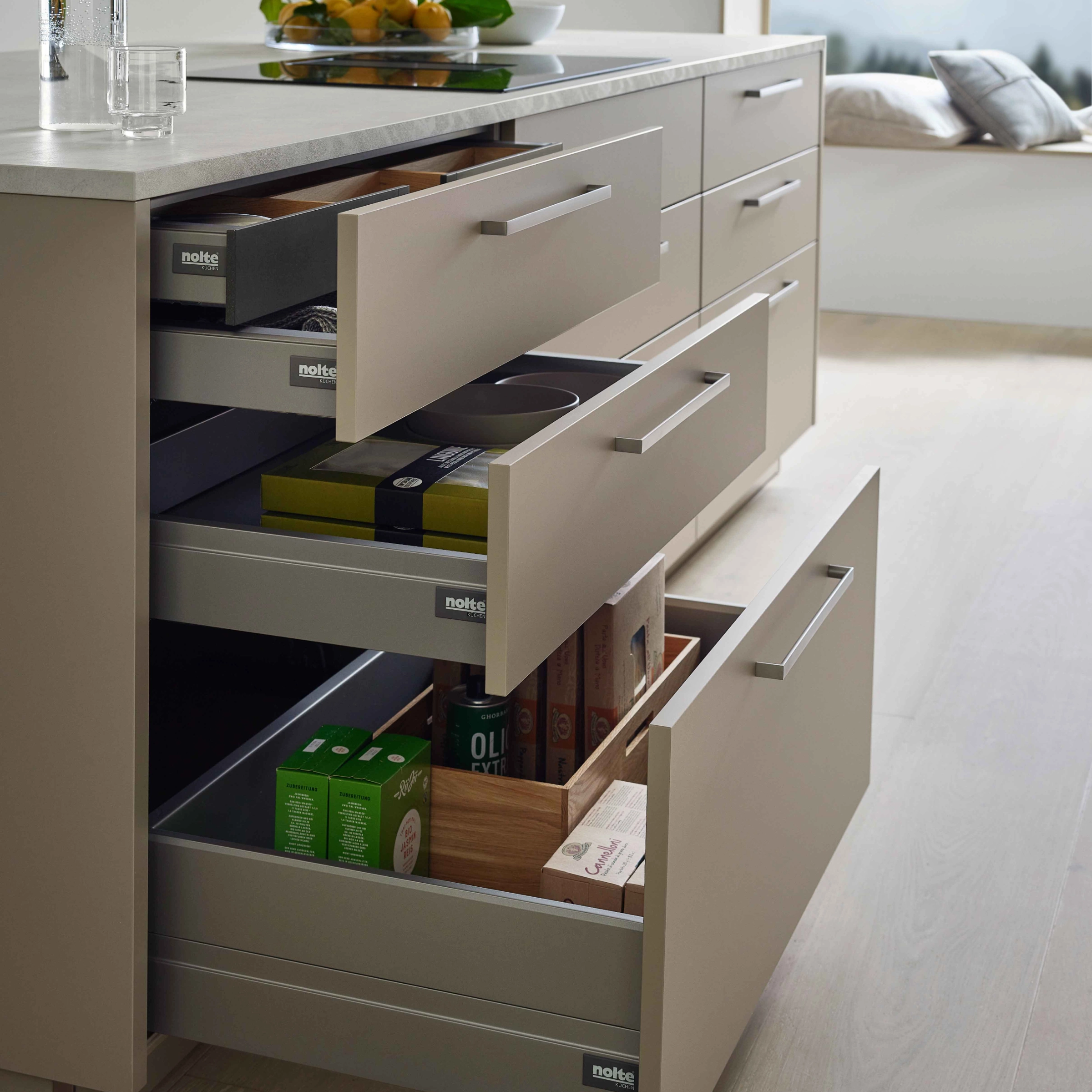 A modern kitchen with open drawers and an island, presented by Nolte Kitchen.