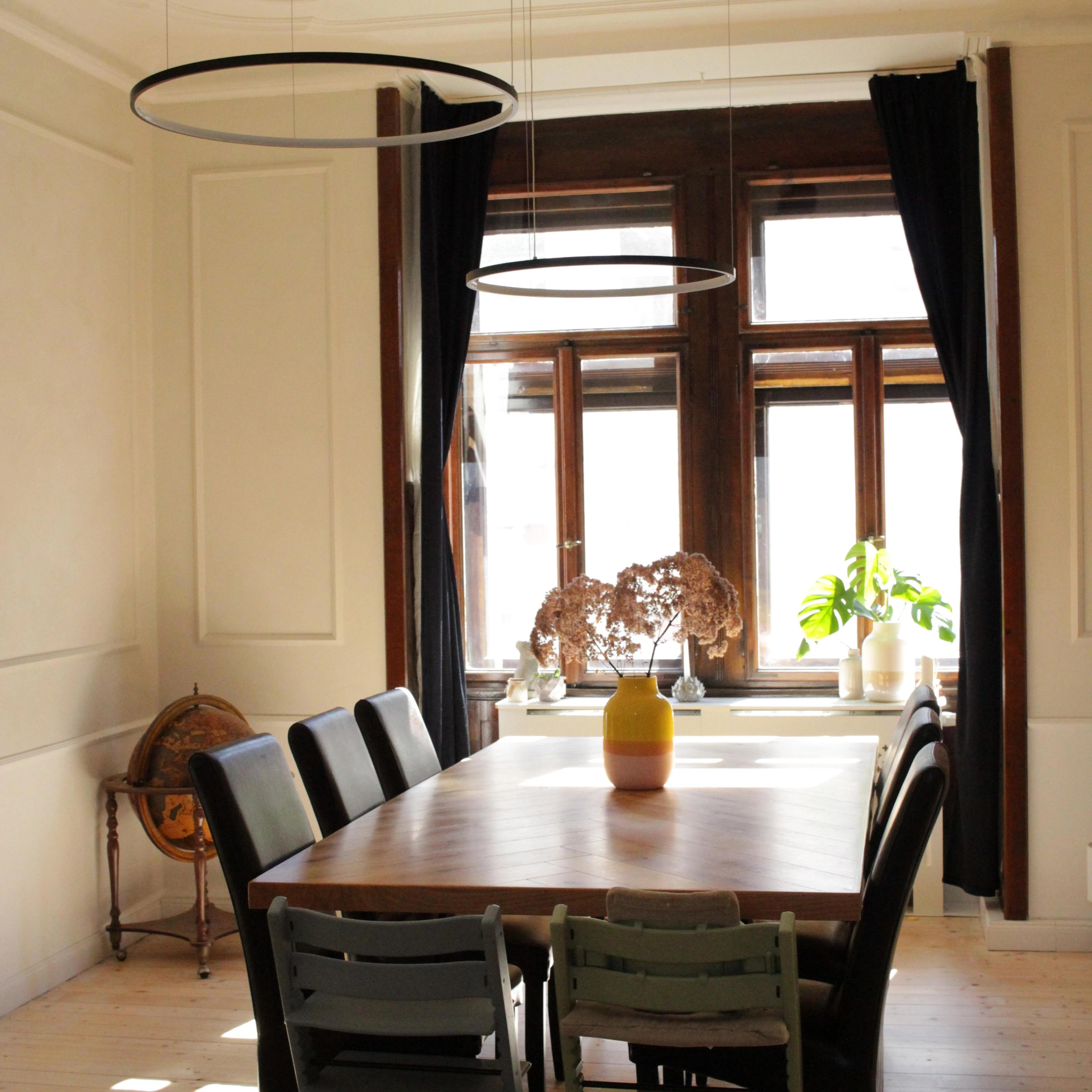 Salle à manger avec longue table en bois, chaises et lampes modernes, assorties à Nolte Living.