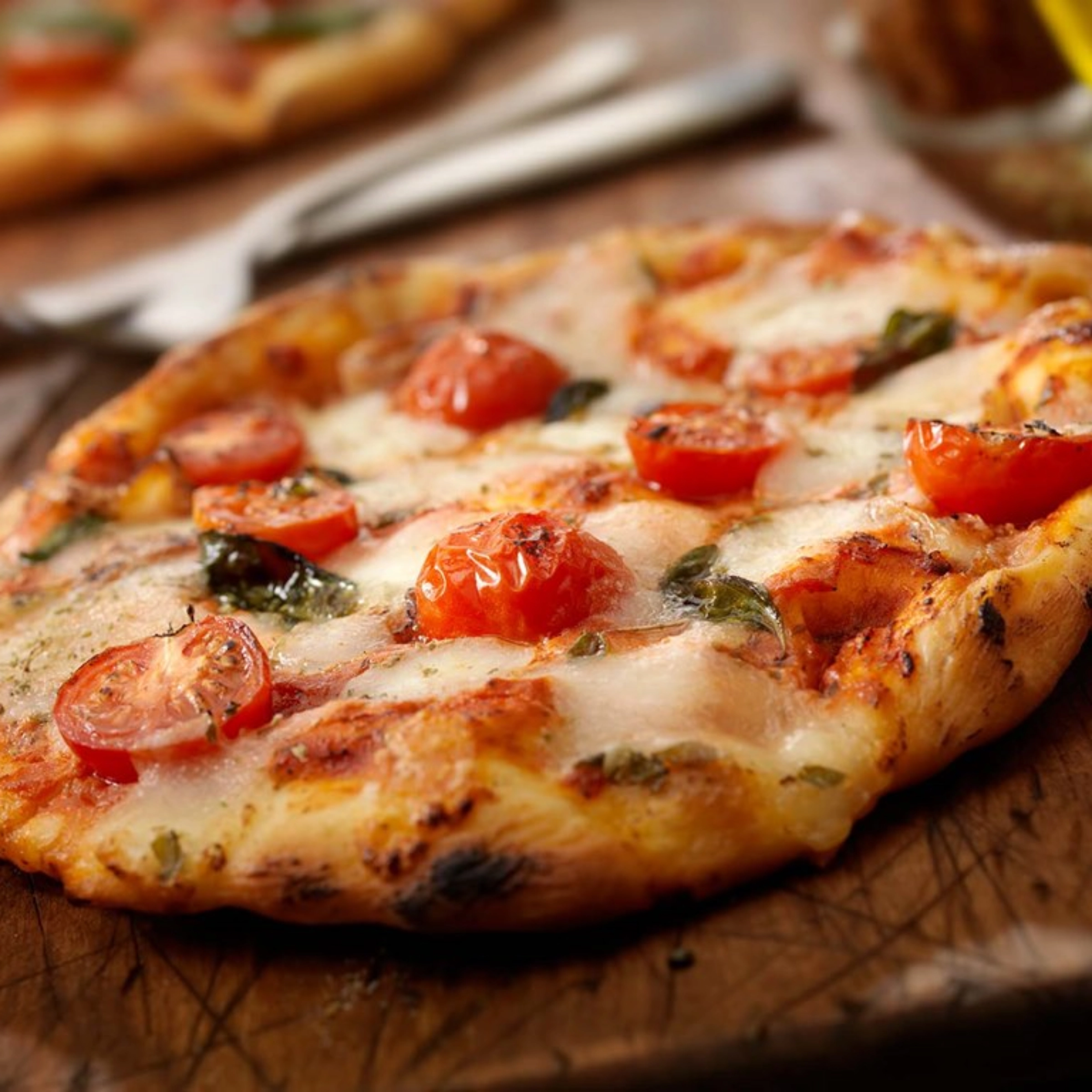 Eine frisch gebackene Pizza mit Tomaten und Basilikum auf einem Holzbrett.