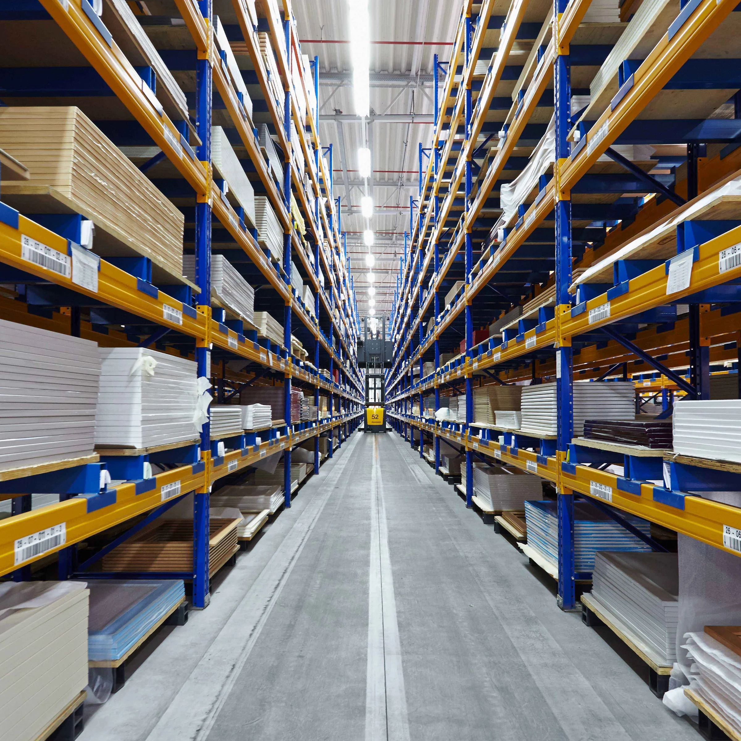 A long aisle in a warehouse with tall shelves full of boards, Nolte Kitchens.