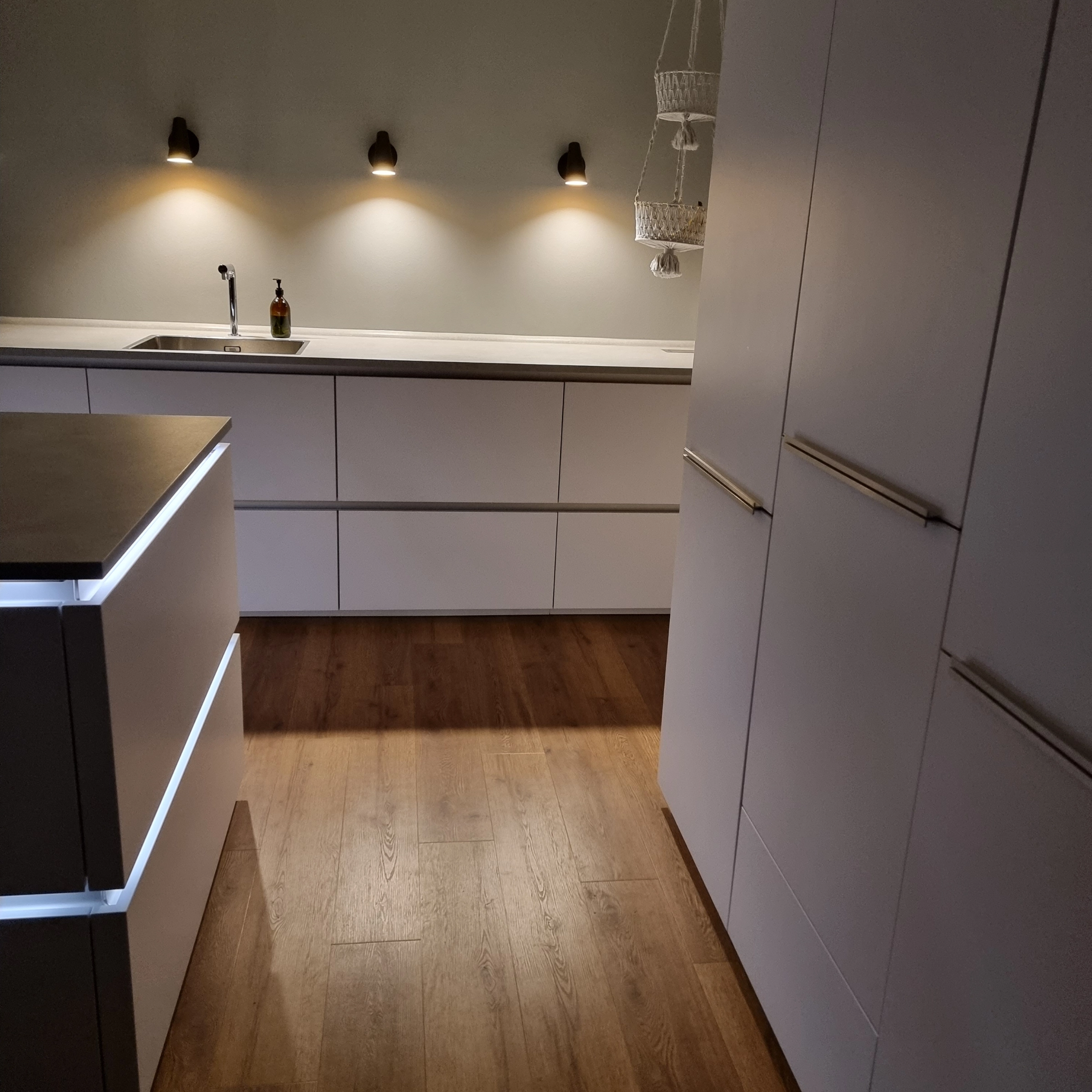 Een moderne keuken met houten vloer en verlichte kasten van Nolte Kitchen.