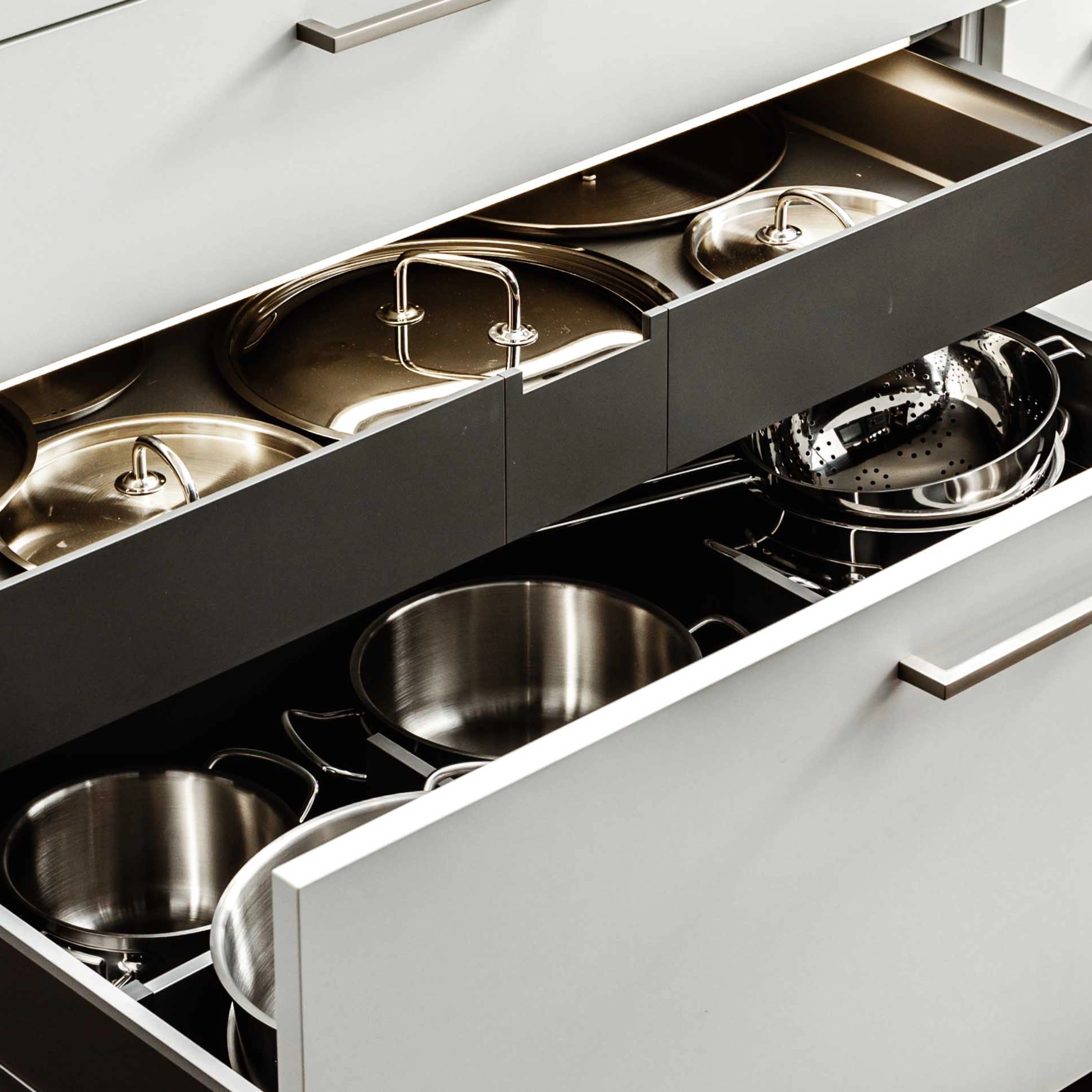 An open kitchen cabinet displaying modern design pots and pans by Nolte Kitchen.