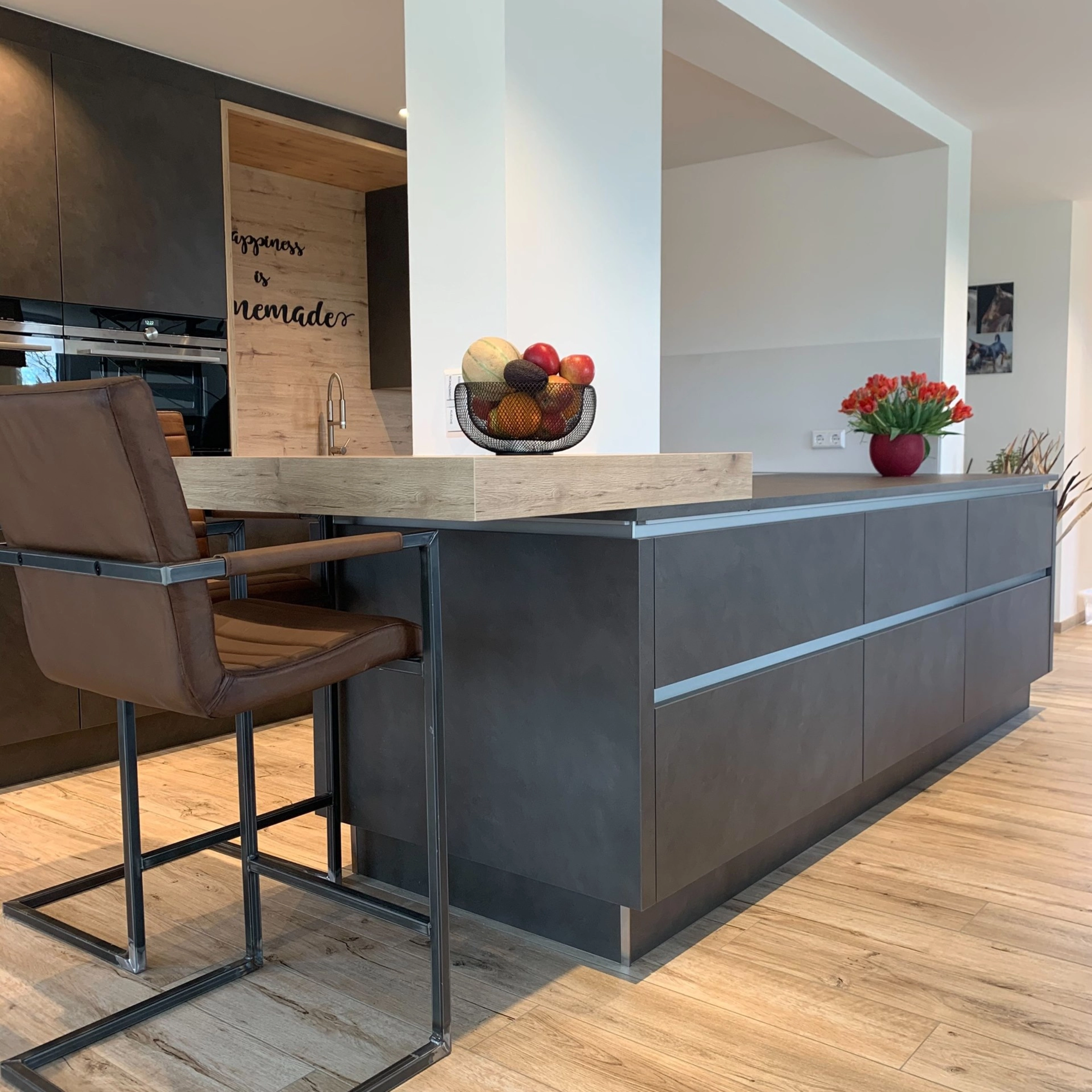 Cucina moderna con isola scura e ciotola di frutta su bancone in legno, sullo sfondo cucine Nolte.
