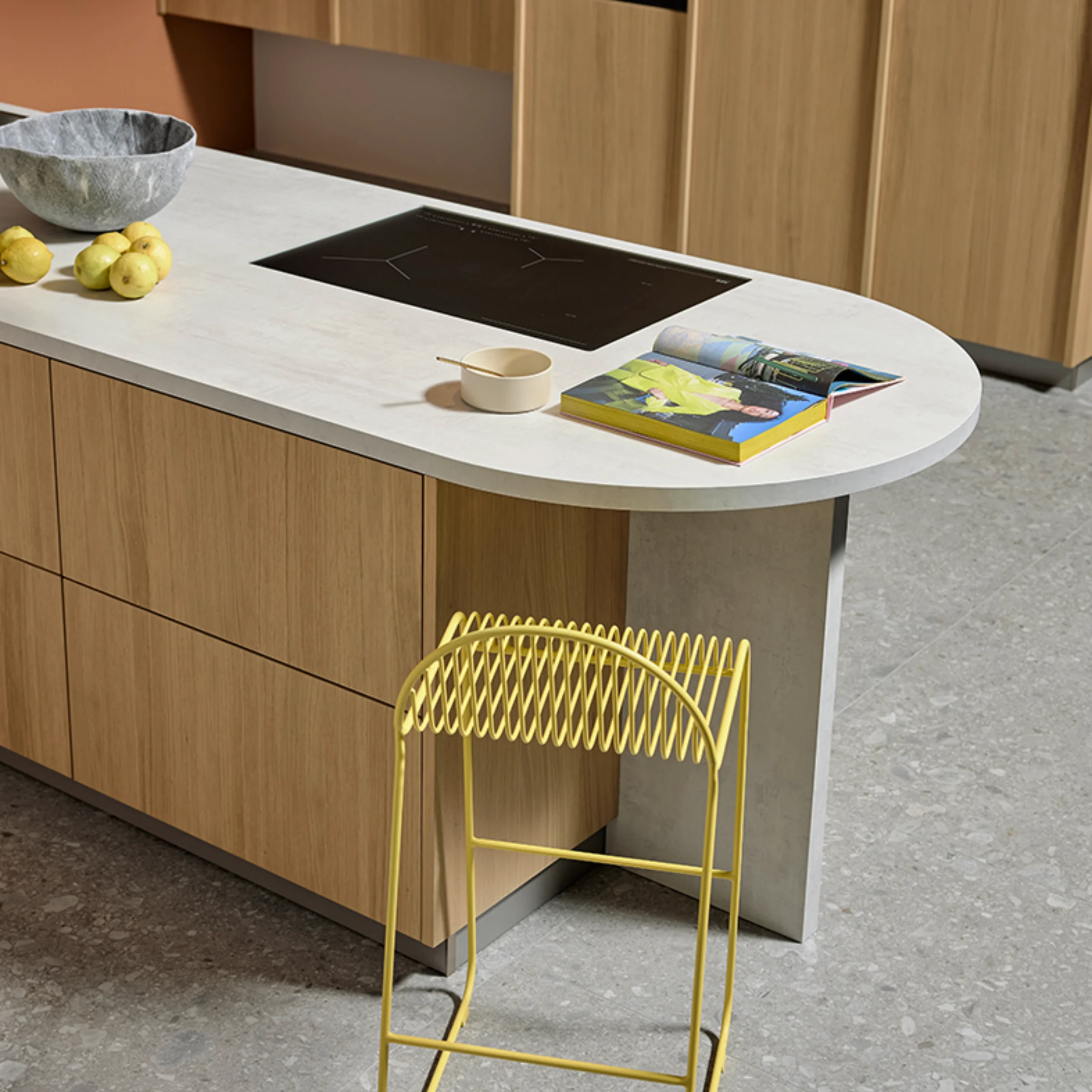 Kochinsel in Eiche Bianco mit heller Arbeitsplatte, eingelassenem Kochfeld und modernen Details. Gelber Barhocker als farblicher Akzent in der nolteneo FLAT Küche.