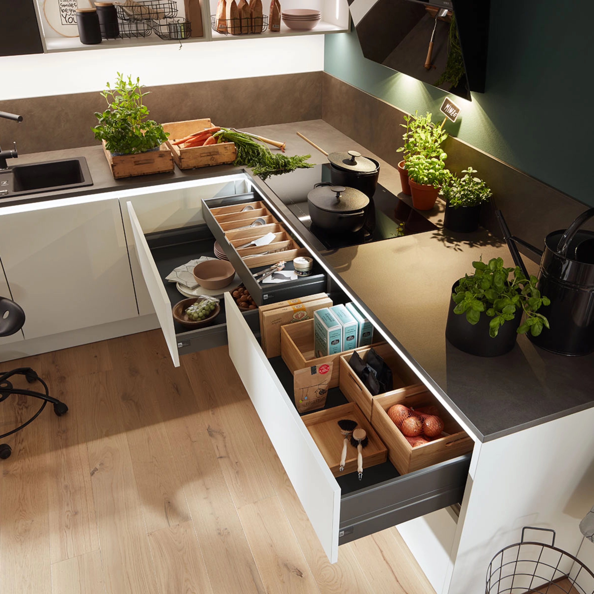 Une cuisine moderne avec tiroirs ouverts et herbes fraîches sur le plan de travail. Nolte Kitchen.