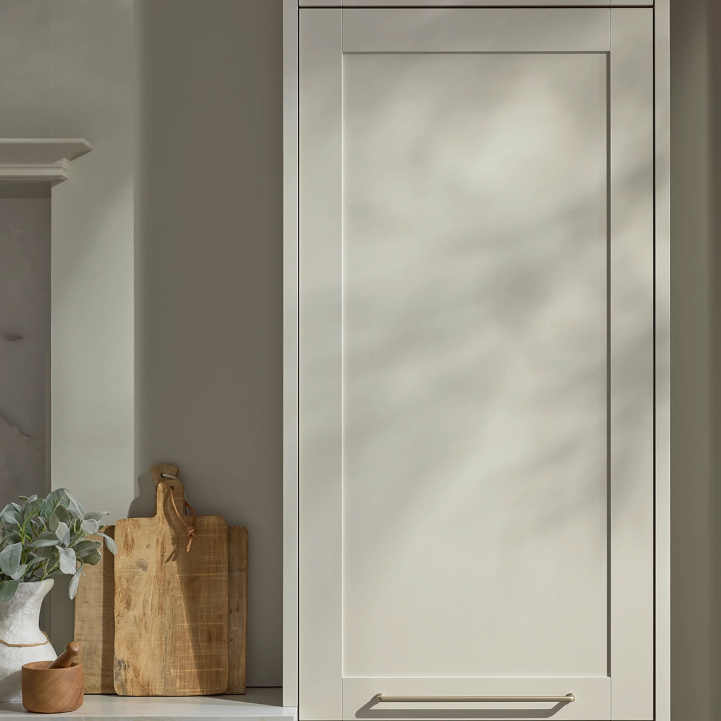 Nahaufnahme eines Hochschranks in Sahara-Ton mit klassischen Rahmenfronten. Holz-Accessoires und sanftes Licht schaffen eine warme, natürliche Atmosphäre in der Nolte CHESTER Küche.