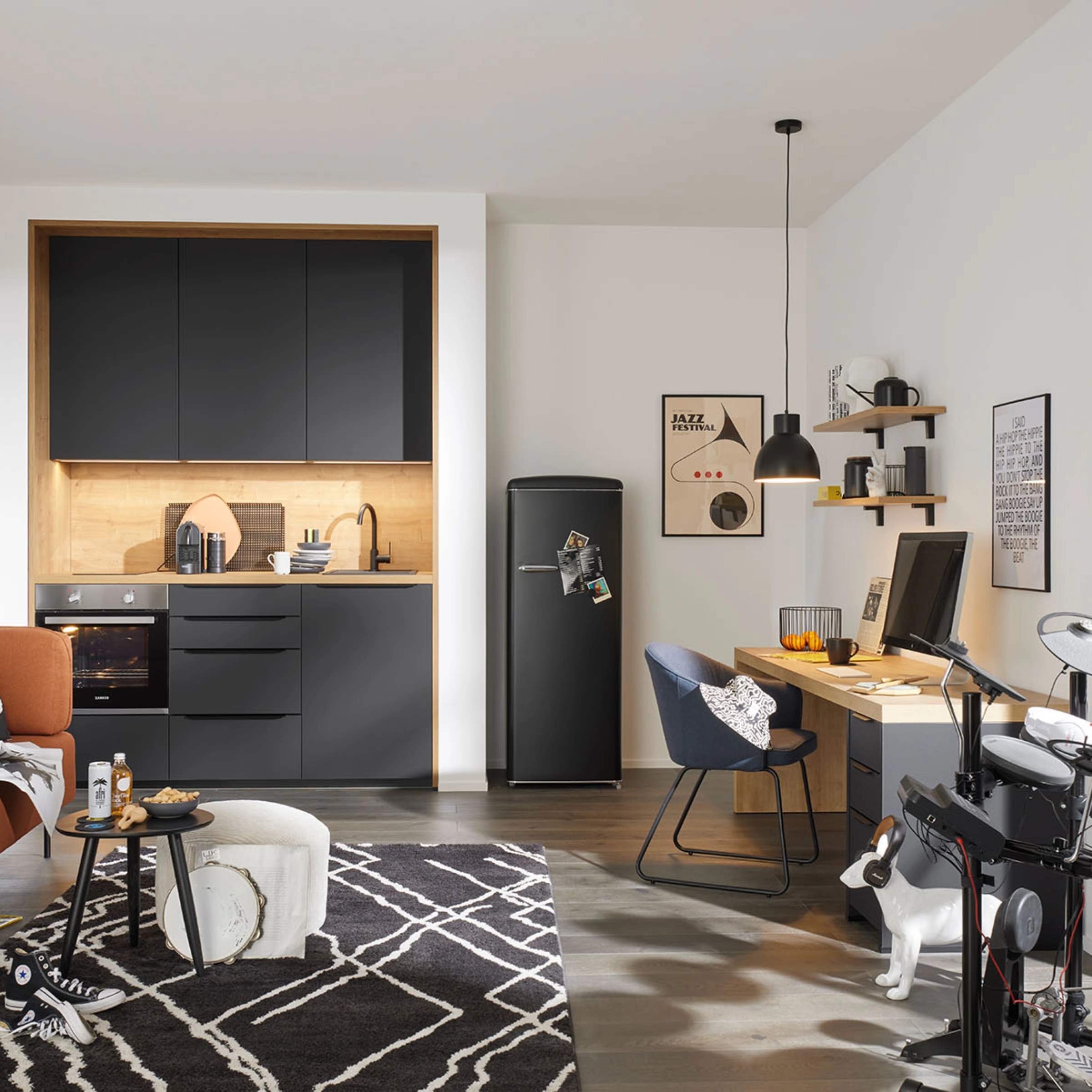 A modern room with a gray Nolte kitchen features a sofa, desk, and electronic drum set.