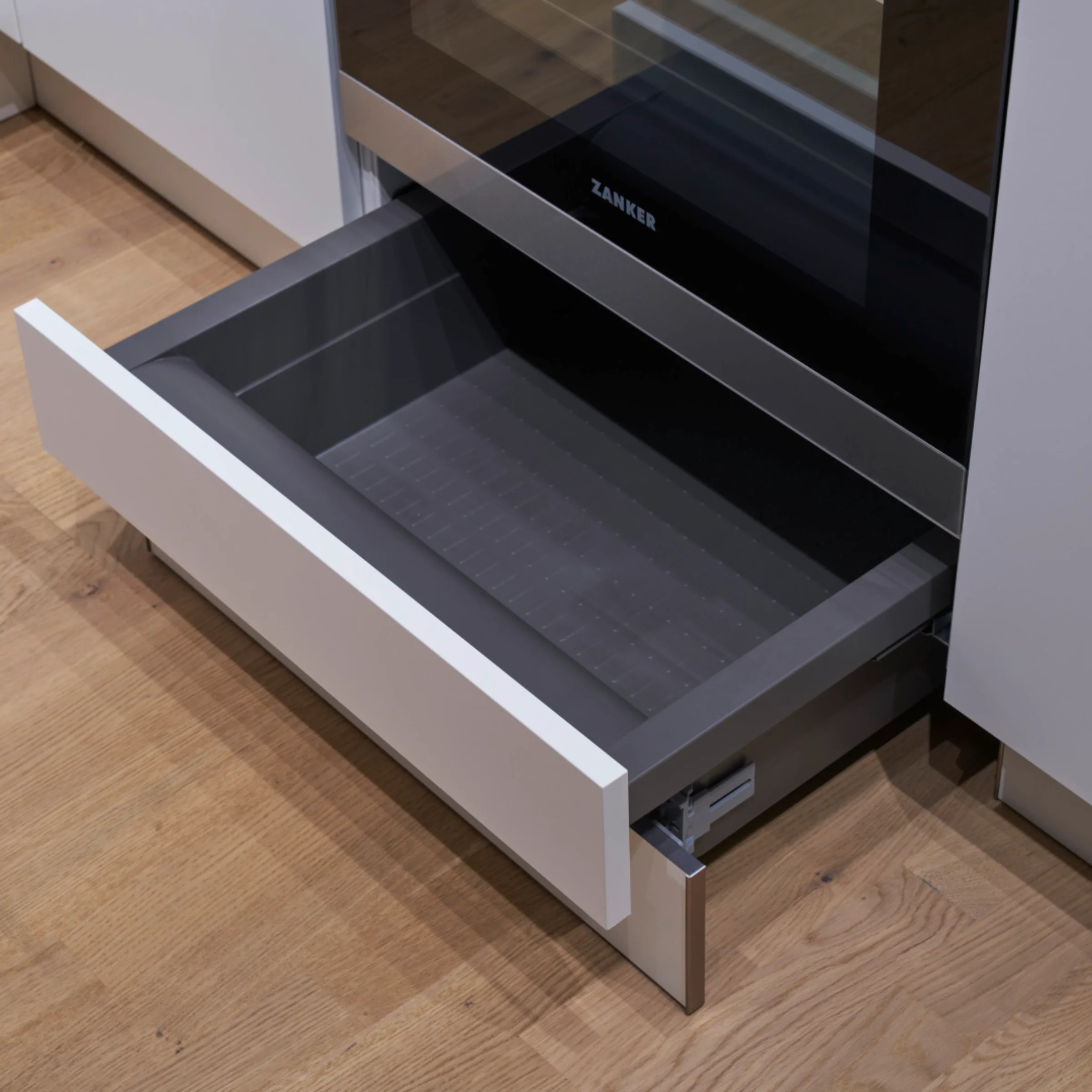 Ein geöffneter Küchenschublade auf Holzboden neben einem Ofen. Nolte Küchen.